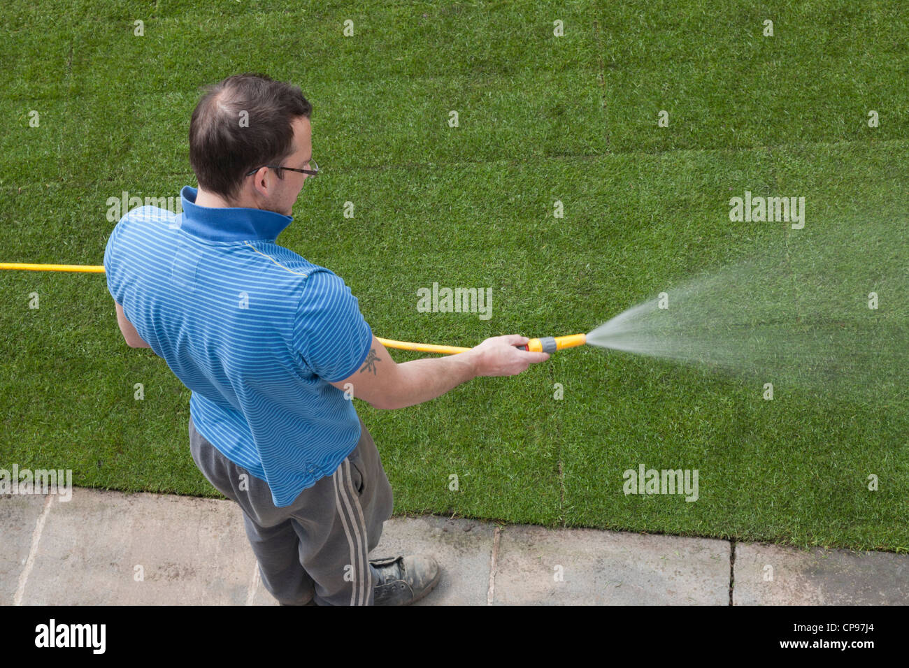Man watering newly laid turf with hosepipe. Stock Photo