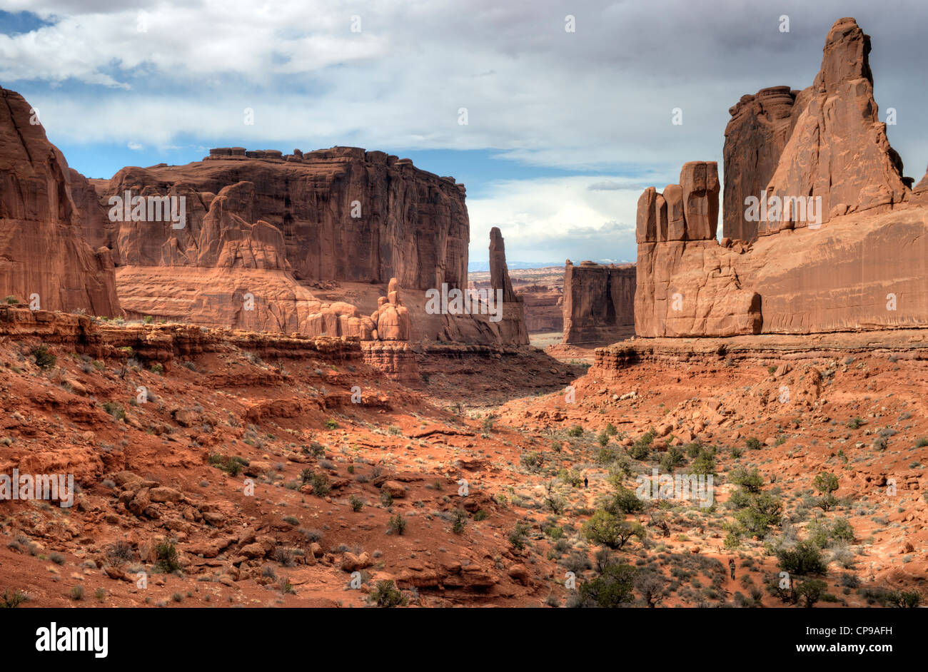 Three hikers ascend the Park Avenue trail in Utah's Arches National Park on a blustery spring day Stock Photo