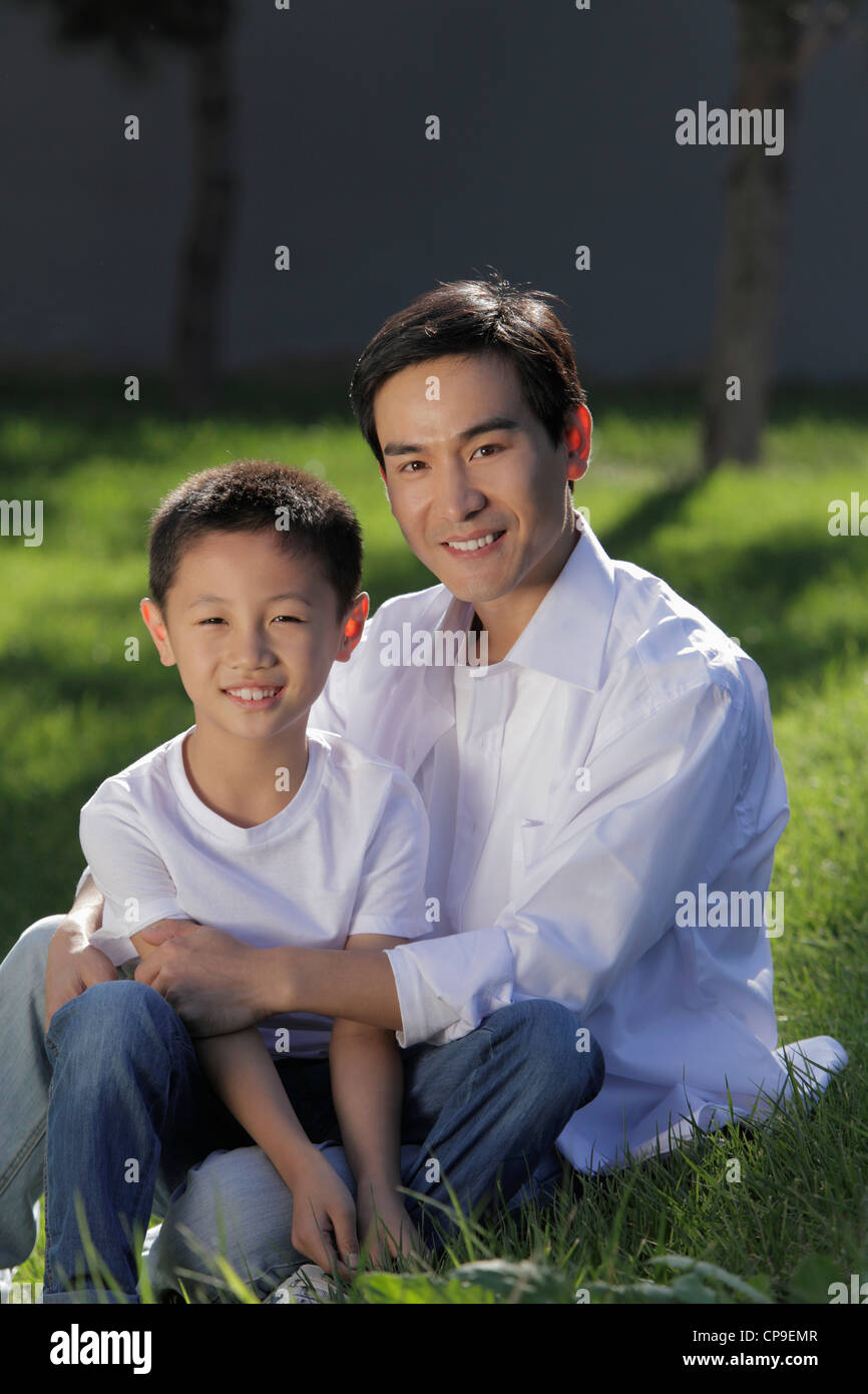 Father and son sitting on grass together smiling Stock Photo - Alamy