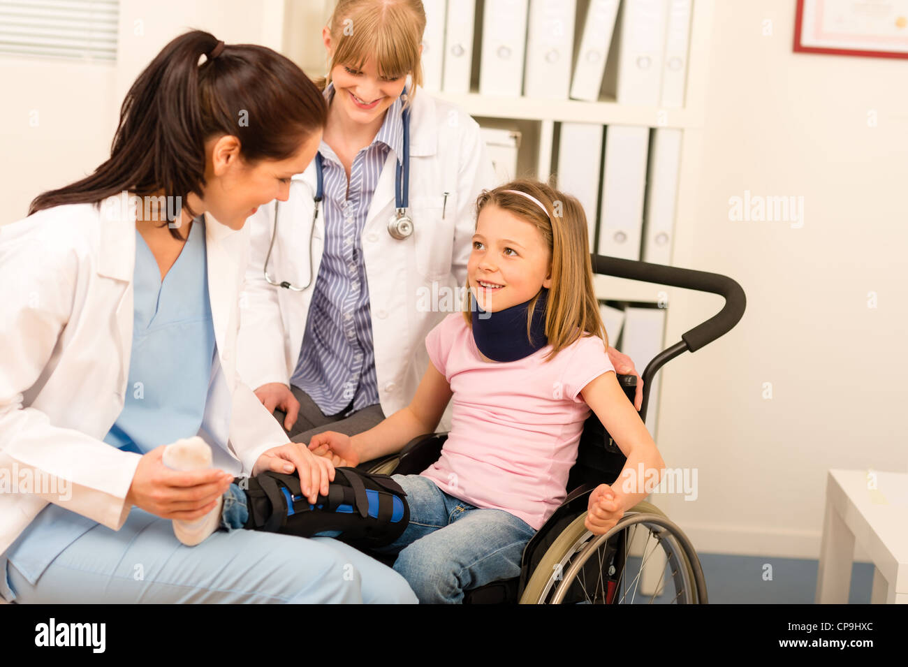 Little injured girl on wheelchair with doctors at medical office Stock Photo