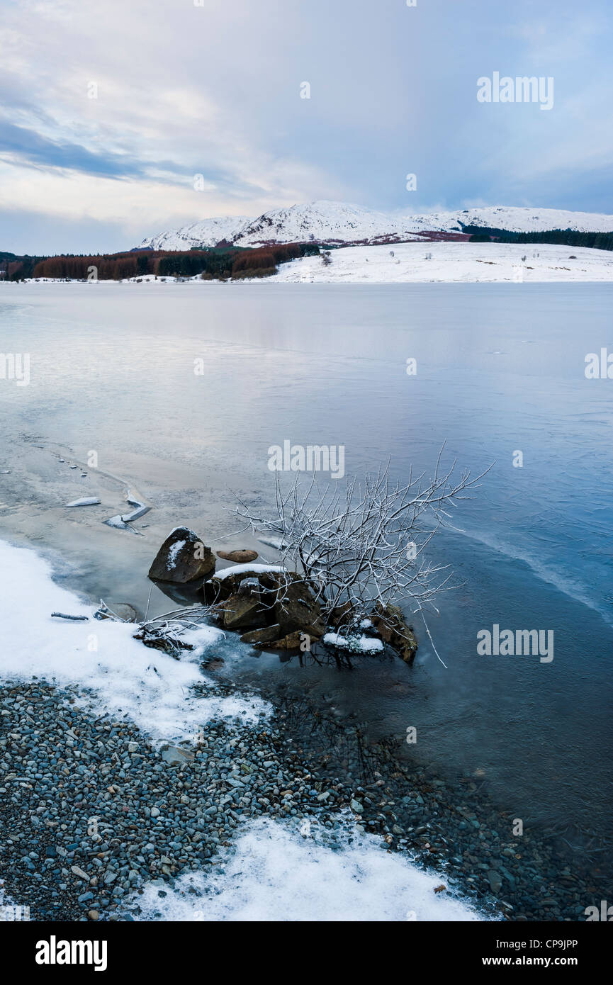 A frozen Clatteringshaws Loch with Craignell in the distance in winter, Galloway Forest Park, Galloway, Scotland, UK Stock Photo