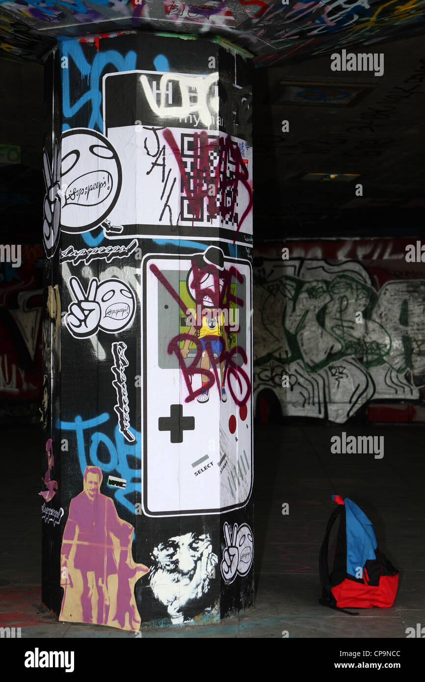 a rucksack next to a pillar full of graffiti, in a skateboard park on the embankment of the river Thames at Waterloo, London Stock Photo