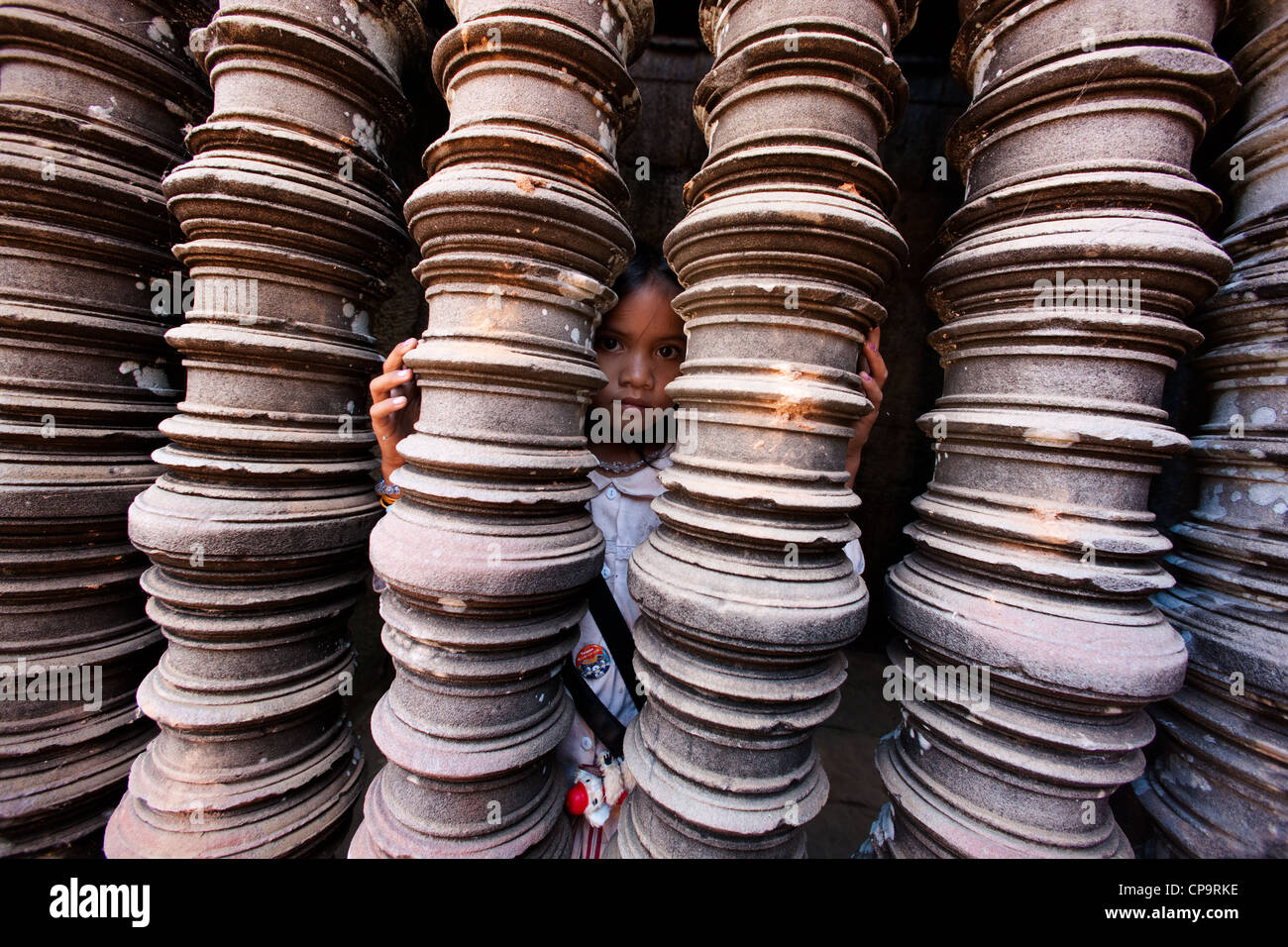 Asian girl looking out from behind a row of sandstone balusters ...