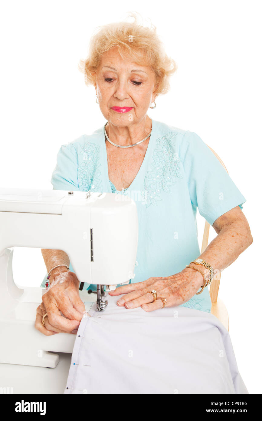 Elderly woman sews with her sewing machine. Isolated on white Stock