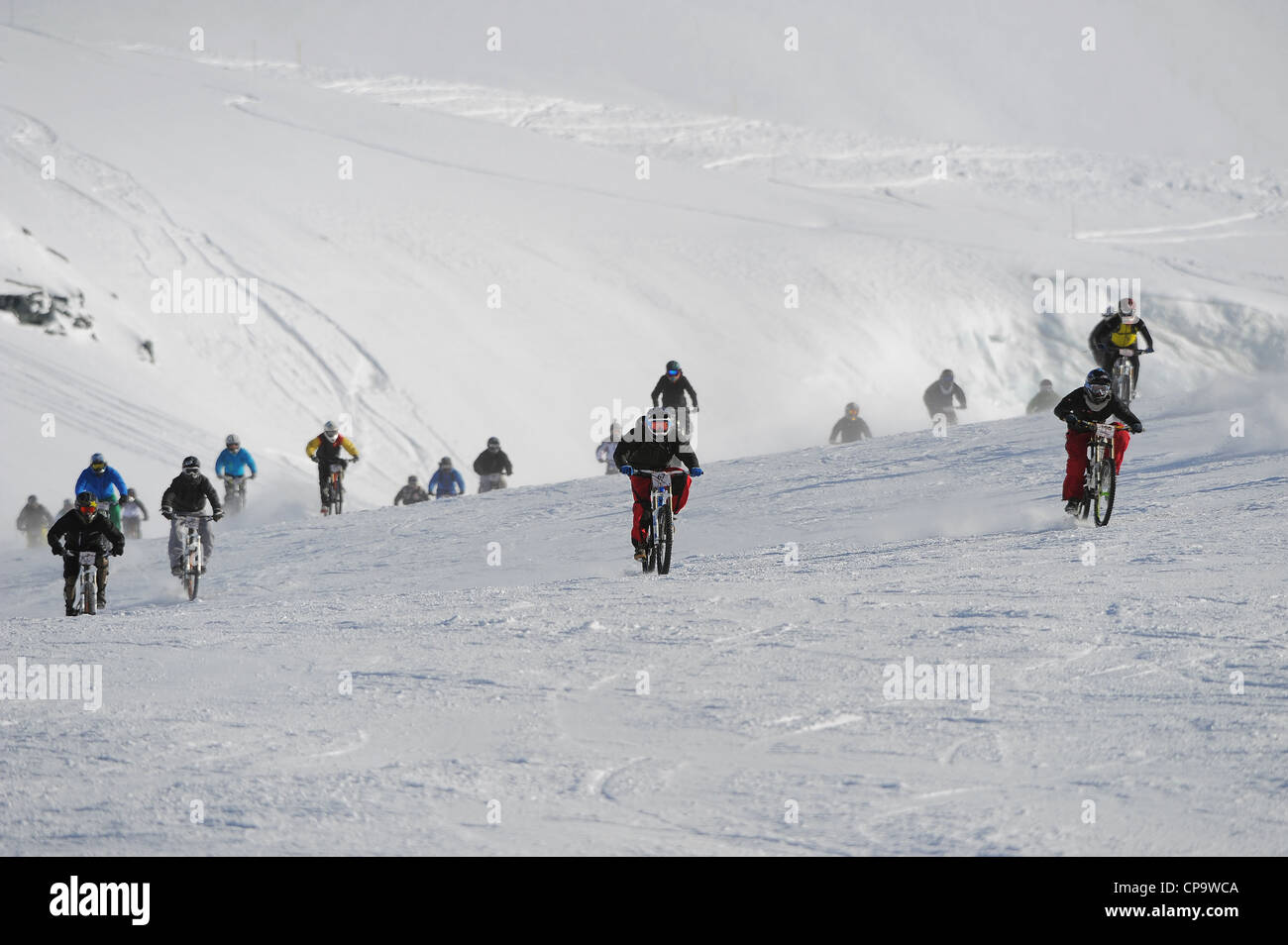 Downhill mountain bikers race at speed on snow during the Saas Fee
