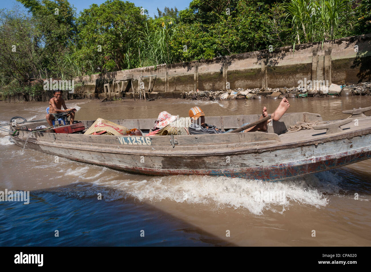 Vietnamese men travelling in a long boat, between Cai Be and Vinh Long, Mekong River Delta, Vietnam Stock Photo