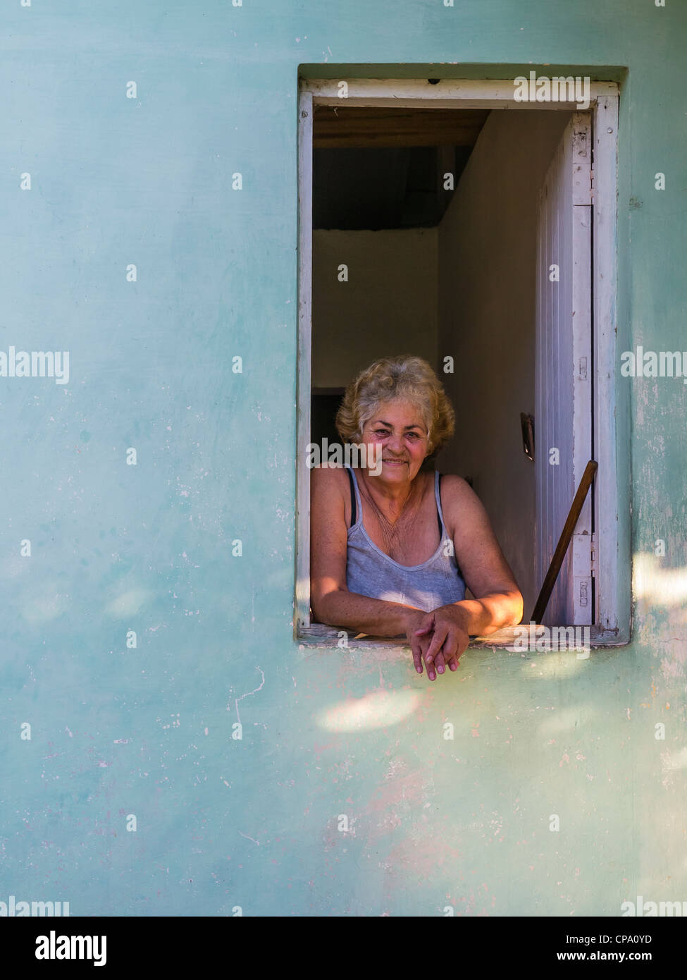 A 60-70 year old Cuban woman looks out of her window and leans her arms on the window sill in Viñales, Cuba. Stock Photo