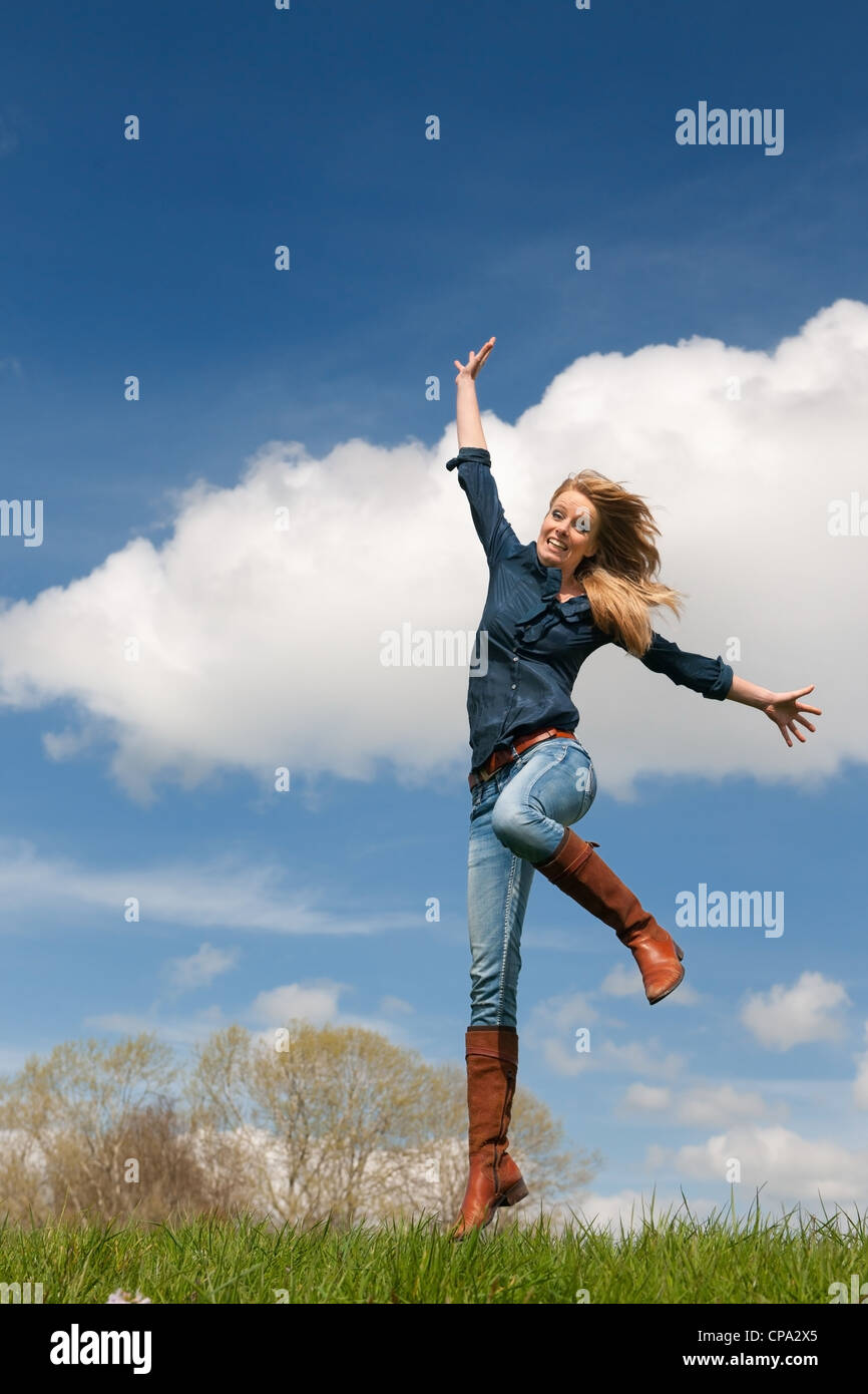 Jumping young blond girl with blue sky and grass Stock Photo - Alamy