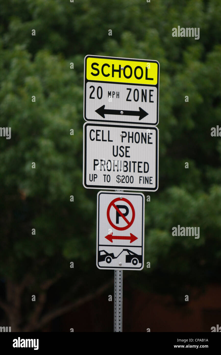 Sign posted by elementary school with school zone speed limit, showing that no parking is allowed and fines for cell phone use Stock Photo