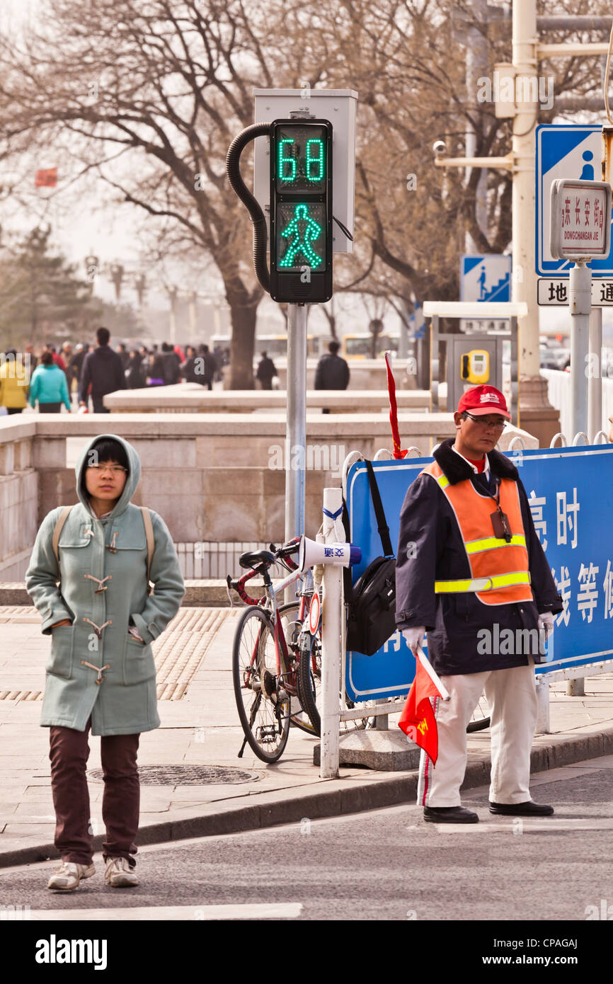 Young woman crossing the road at a pedestrian crossing with green man and traffic warden, Chang'an Avenue, Beijing, China. Stock Photo