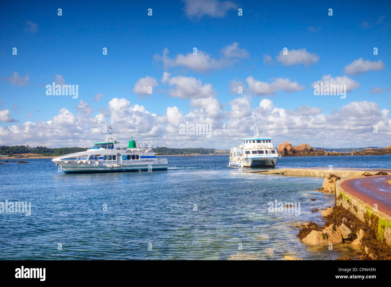 Ferry and tourist boat manoeuvering at the low tide jetty of the main harbour on Ile de Brehat, Brittany, France. Stock Photo