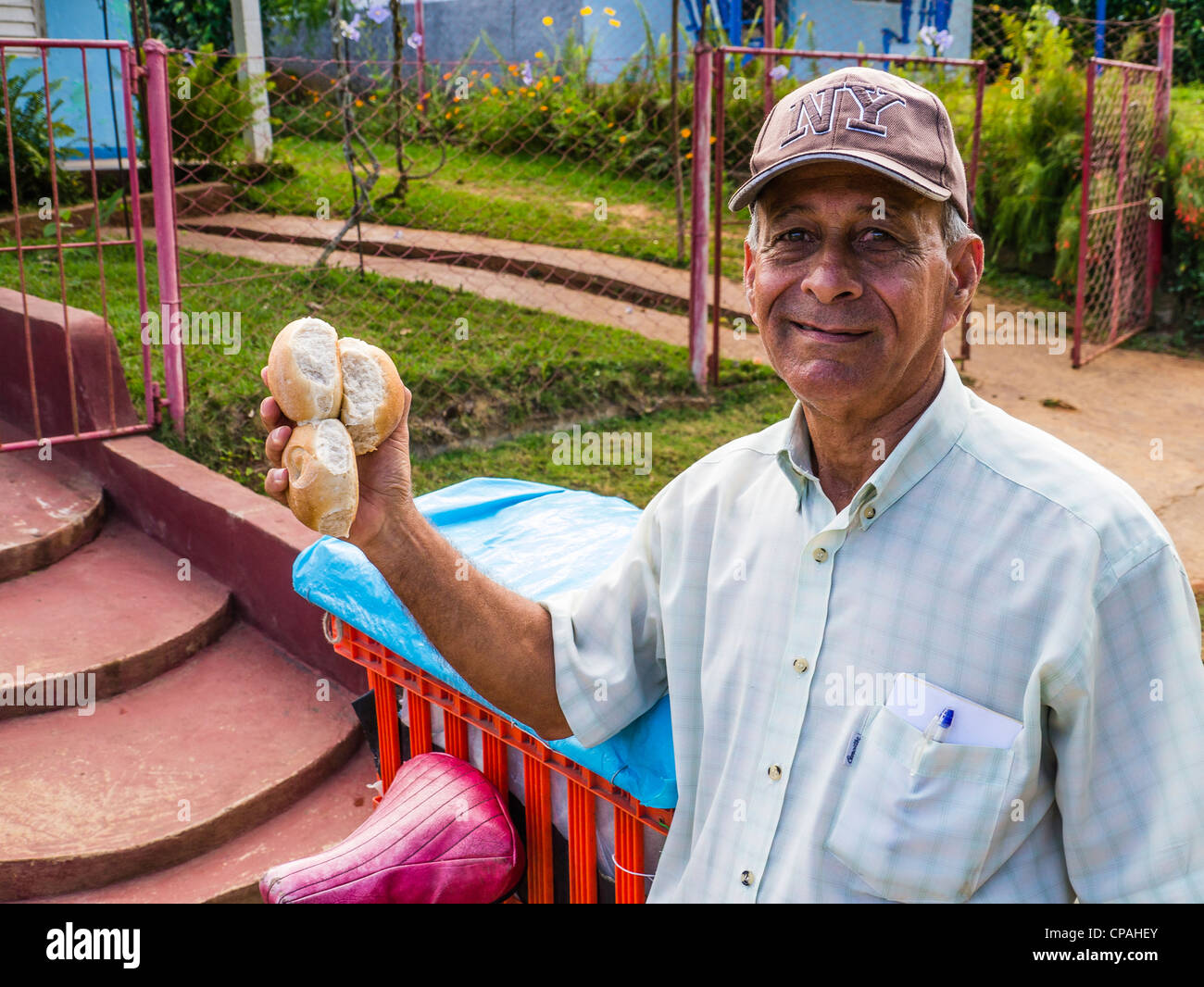 A 50-60 year old Cuban Hispanic bread vendor holds three freshly baked rolls in his hand as he delivers them in Viñales, Cuba. Stock Photo