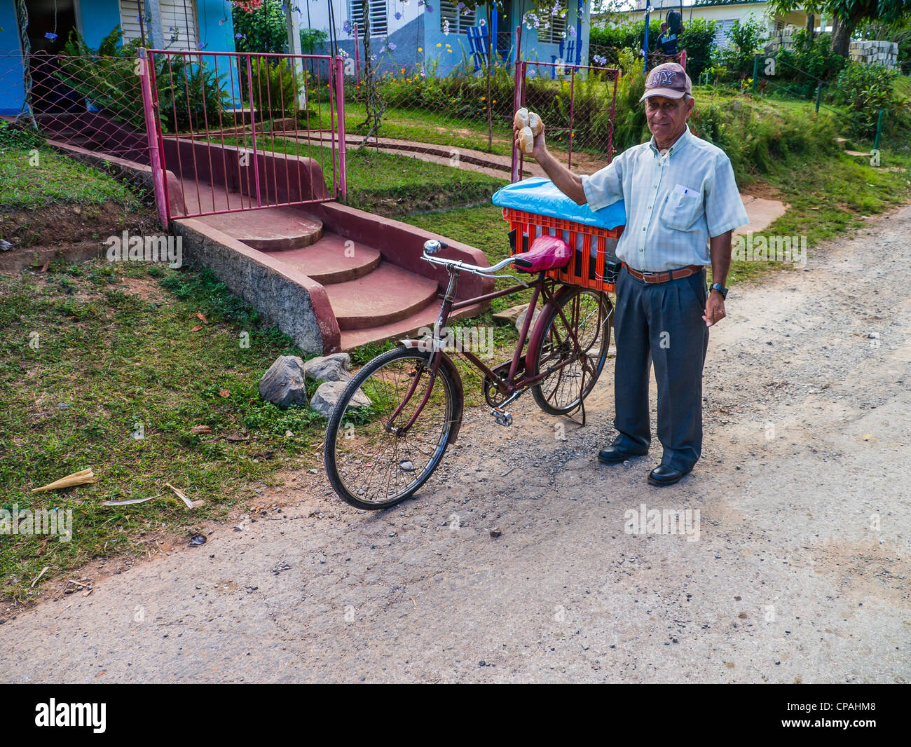 A Cuban Hispanic bread vendor holds freshly baked rolls in his hand as he delivers them on his bicycle in rural Viñales, Cuba. Stock Photo