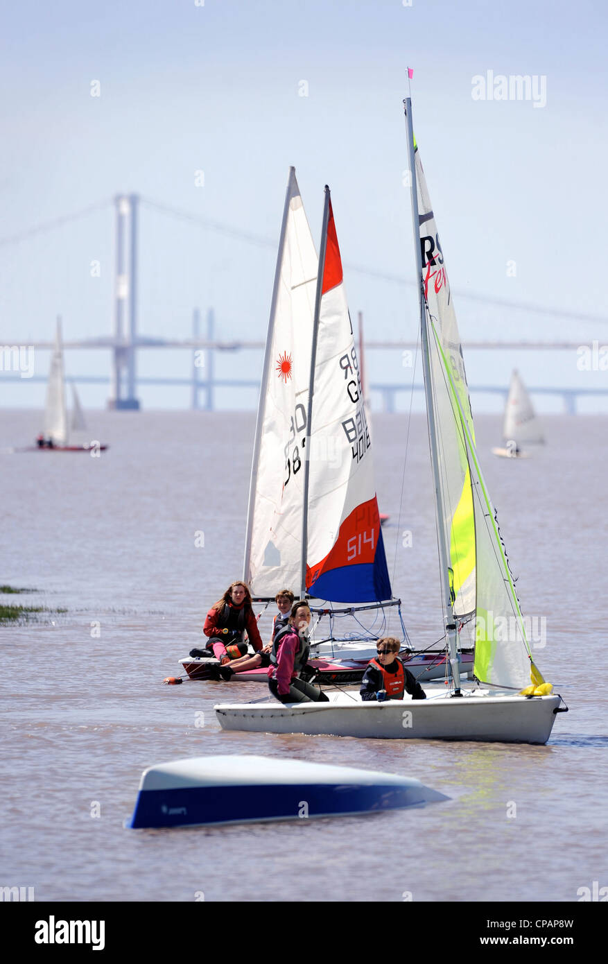 Sailers approach an upturned boat at a regatta on the River Severn with the first Severn Bridge nearest and second Severn crossi Stock Photo