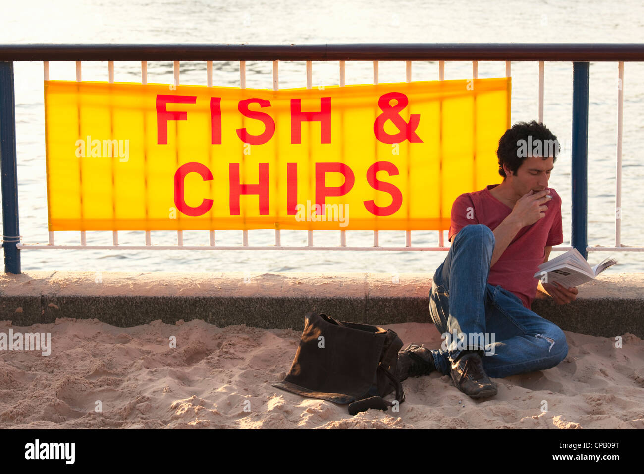 Man reading book on South bank in front of Fish and Chips sign; London; England Stock Photo