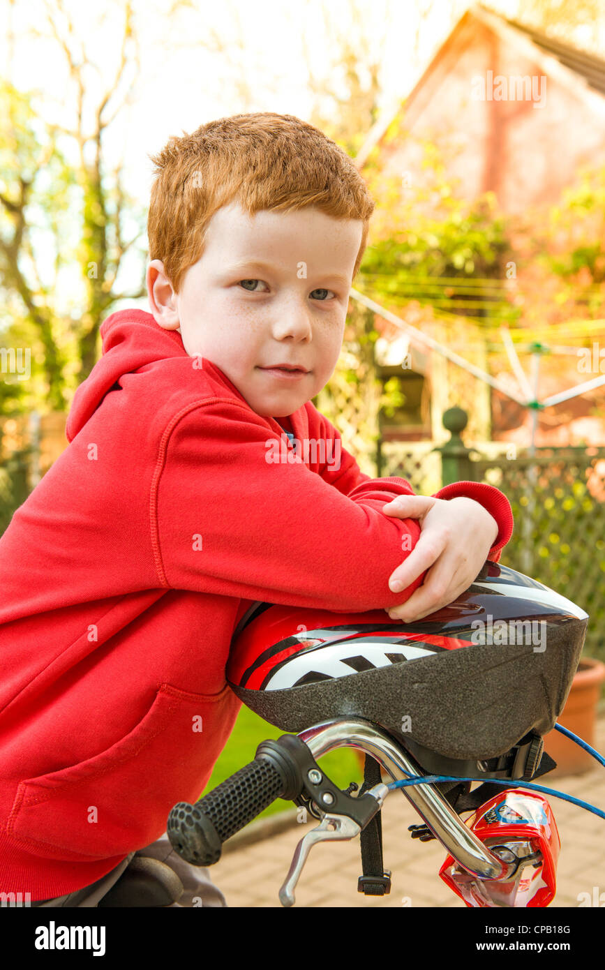 Little boy on his bike in his garden, looking to camera. Stock Photo