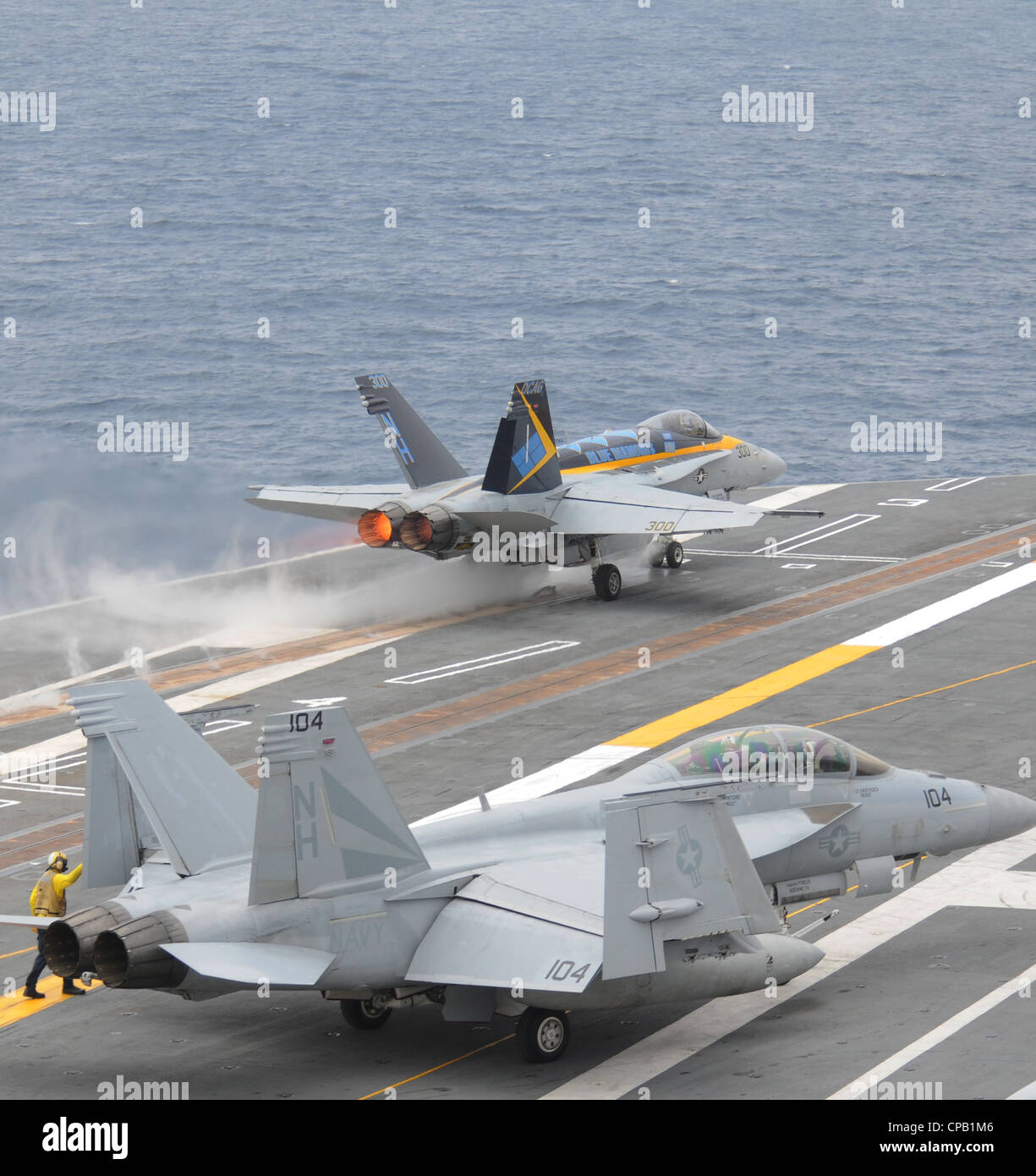 An F/A-18C Hornet assigned to the Blue Diamonds of Strike Fighter Squadron (VFA) 146 launches from the aircraft carrier USS Nimitz (CVN 68) as an F/A-18F Super Hornet assigned to the Black Knights of Strike Fighter Squadron (VFA) 154 taxies to catapult one in preparation for launch from the flight deck. Nimitz is conducting carrier qualifications off the coast of southern California. Stock Photo