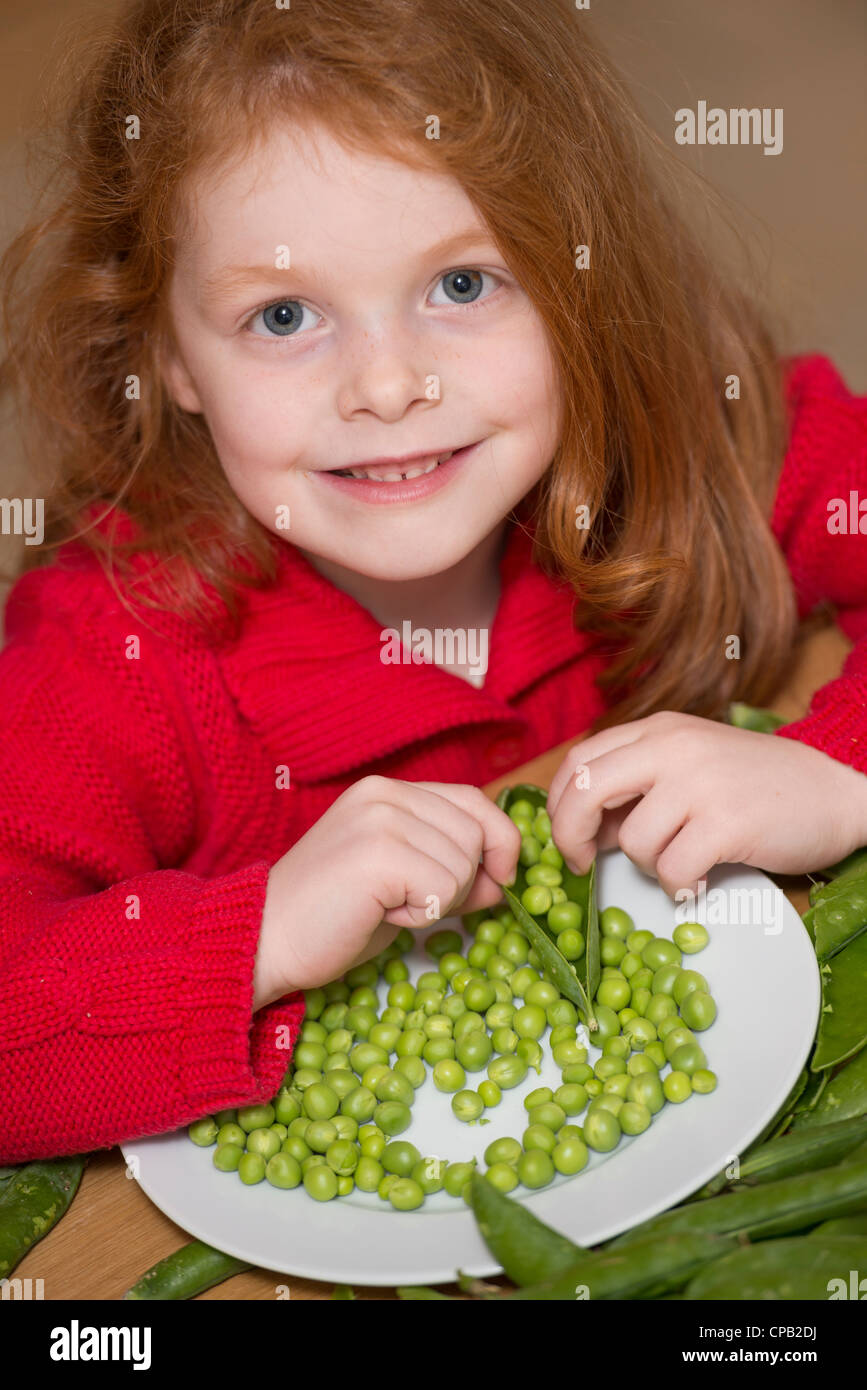 Child shelling peas on a kitchen table Stock Photo
