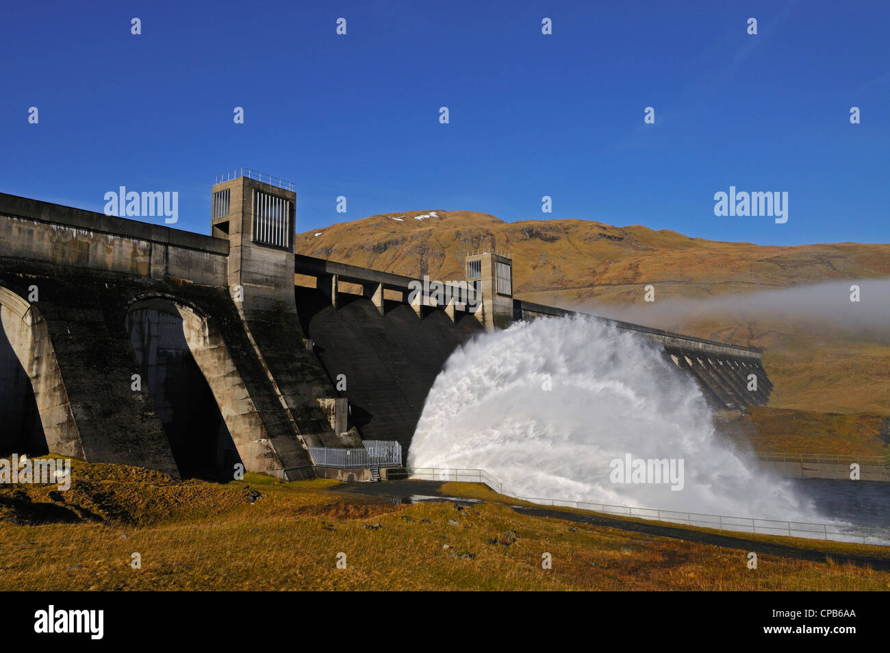 Glen Lyon HydroElectric dam venting water with a background of misty hills and blue sky, Perthshire, Scotland, UK. Stock Photo