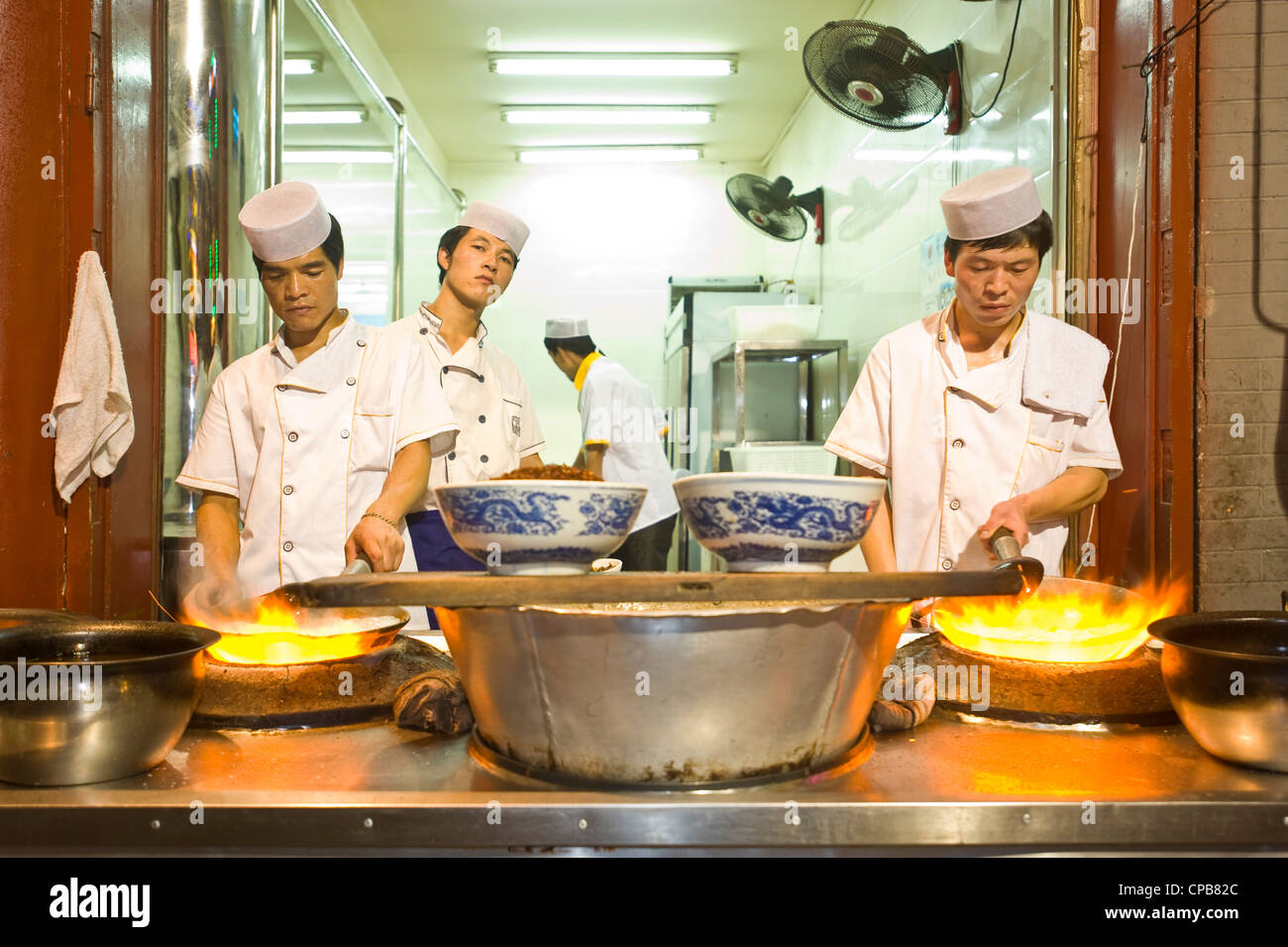 Chinese chefs cooking over a traditional gas burning stove and wok at a restaurant in Moslem Street (Huimin Jie) in Xian. Stock Photo