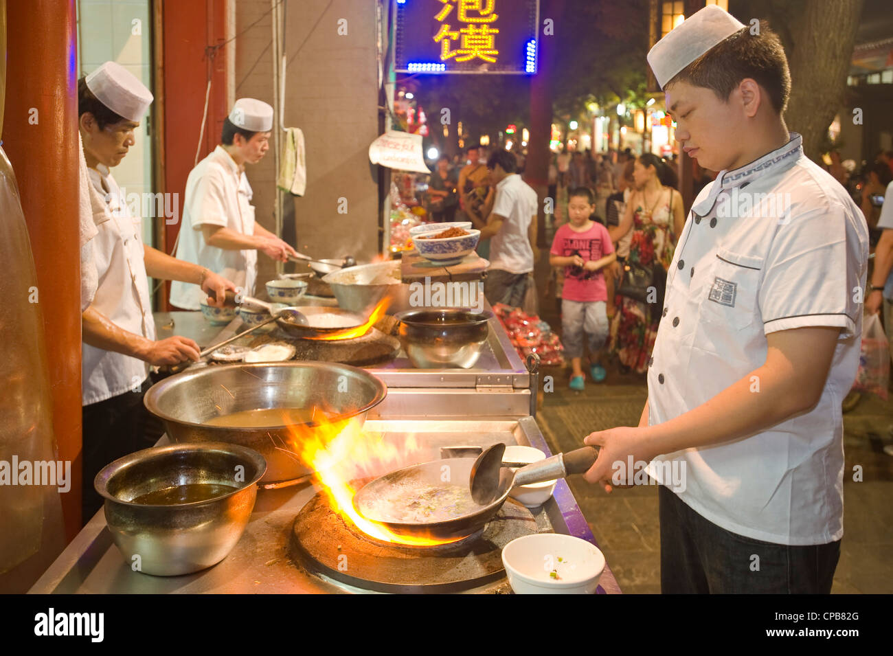 Chinese chefs cooking over a traditional gas burning stove and wok at a restaurant in Moslem Street (Huimin Jie) in Xian. Stock Photo