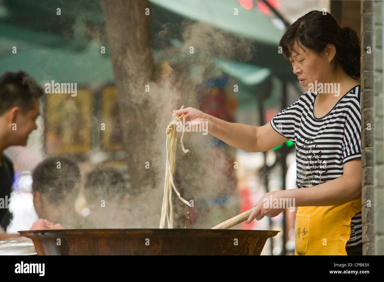 An Chinese lady cooking noodles at an outside food stall of Moslem Street (Huimin Jie) in Xian. Stock Photo