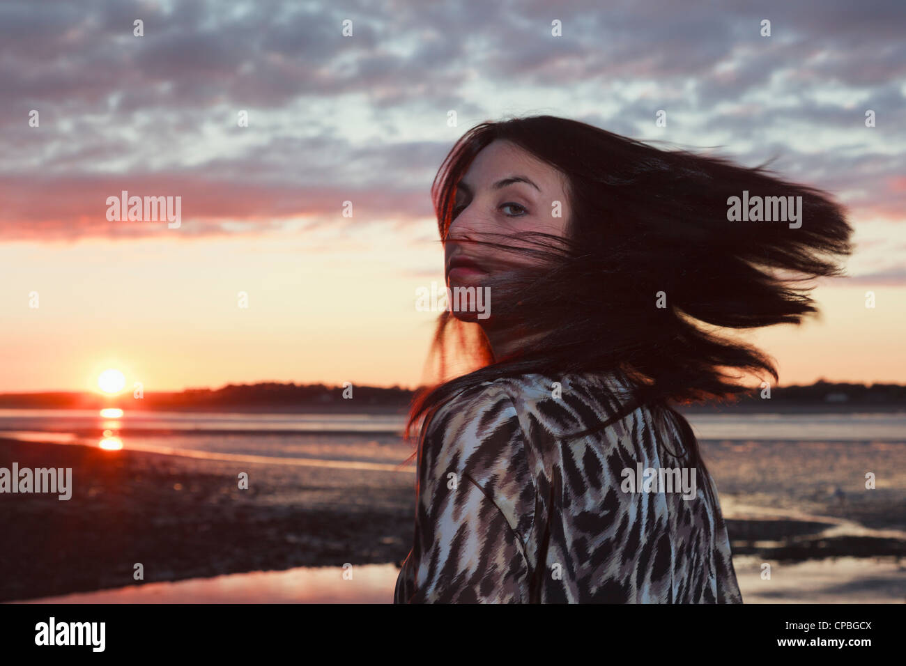 Portrait of a young woman swishing her hair at the coast with the sunset over the Menai Strait as backdrop. Wales UK Stock Photo