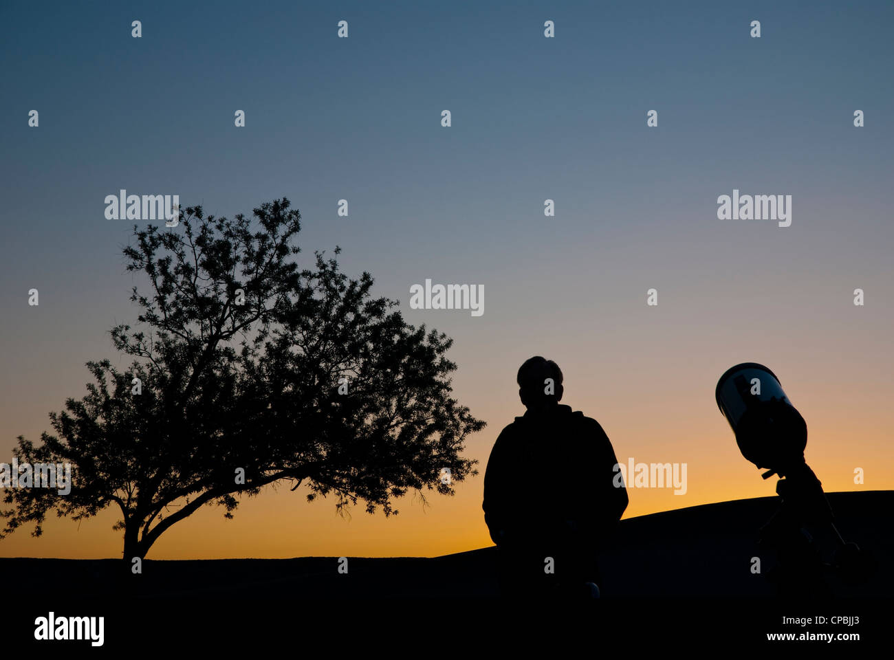 silhouette of an Astronomer and his telescope waiting for the sun to go down Stock Photo