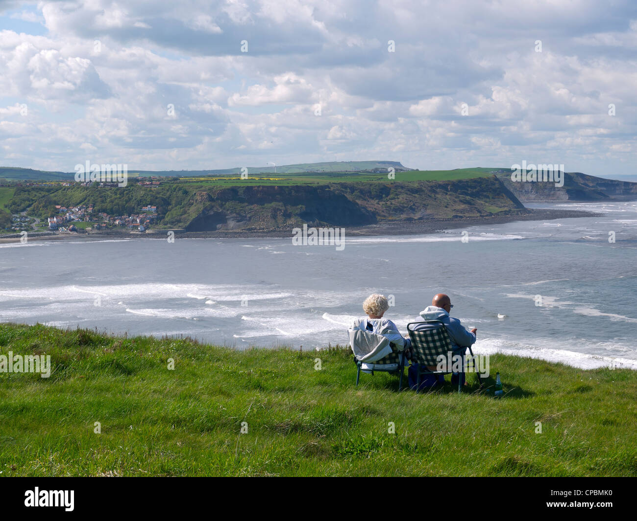 A man and a woman enjoy spring sunshine on the cliff top at Kettleness overlooking Runswick Bay North Yorkshire Stock Photo