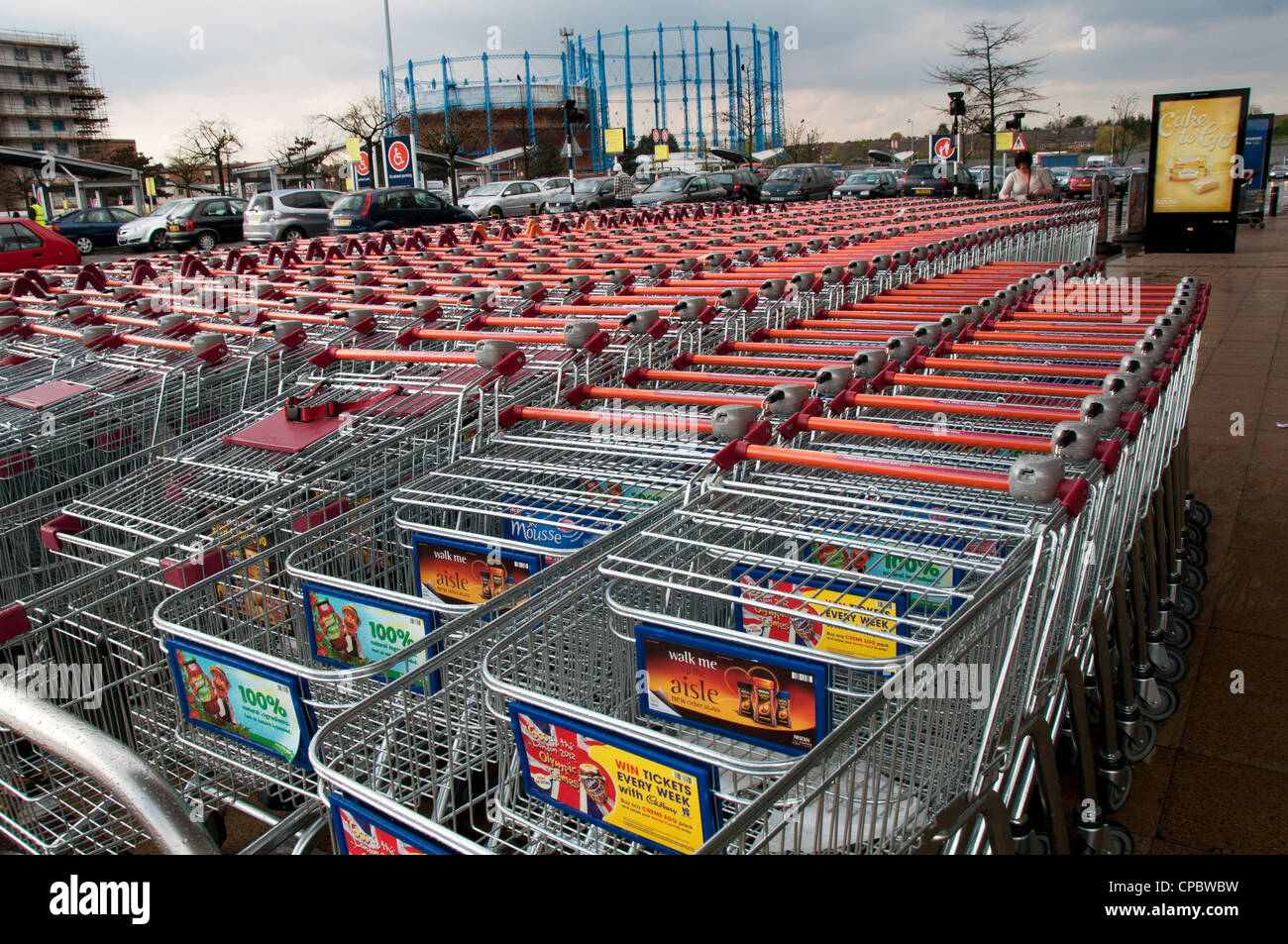 Empty trolleys lined up outside supermarket with gasometer in background Stock Photo