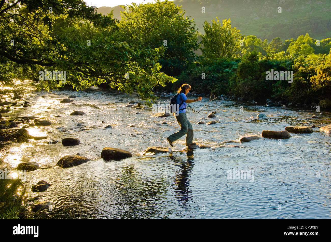 Walker crossing stepping stones on the River Esk near Boot in the English Lake District Stock Photo