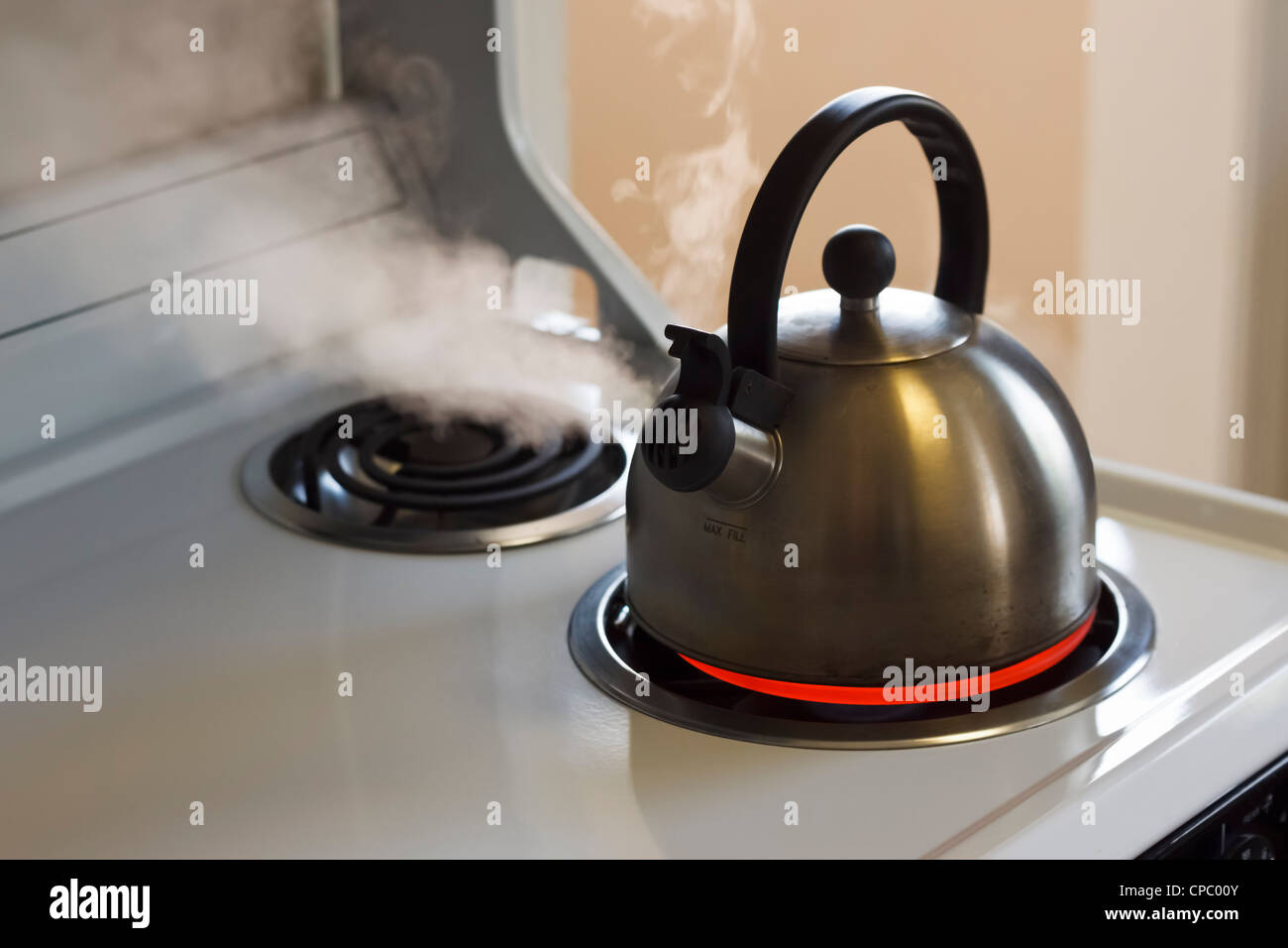 Stainless steel tea kettle coming to a boil on a white stove top Stock