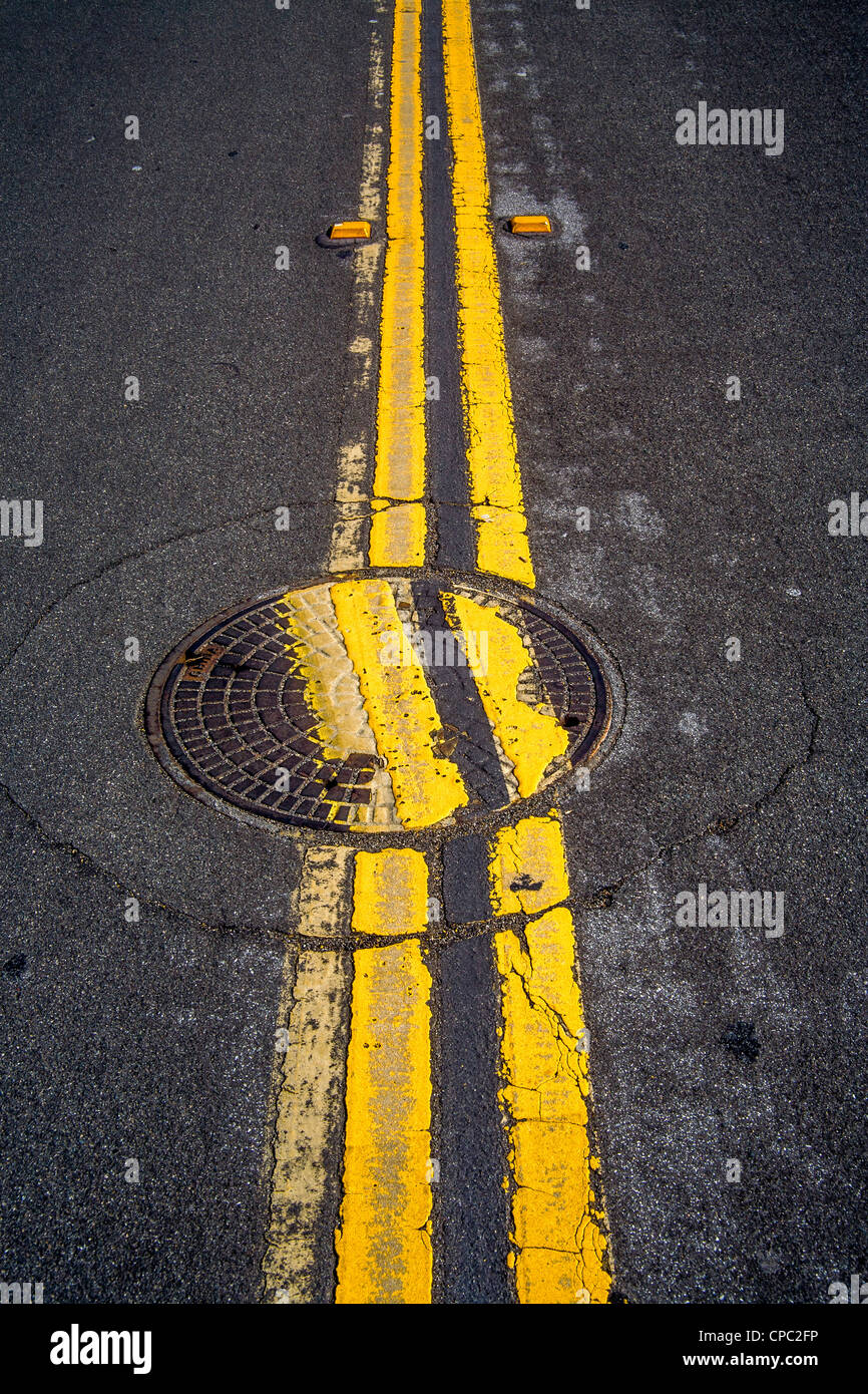 A carelessly replaced manhole cover interrupts two parallel lines on a street in San Clemente, CA. Stock Photo