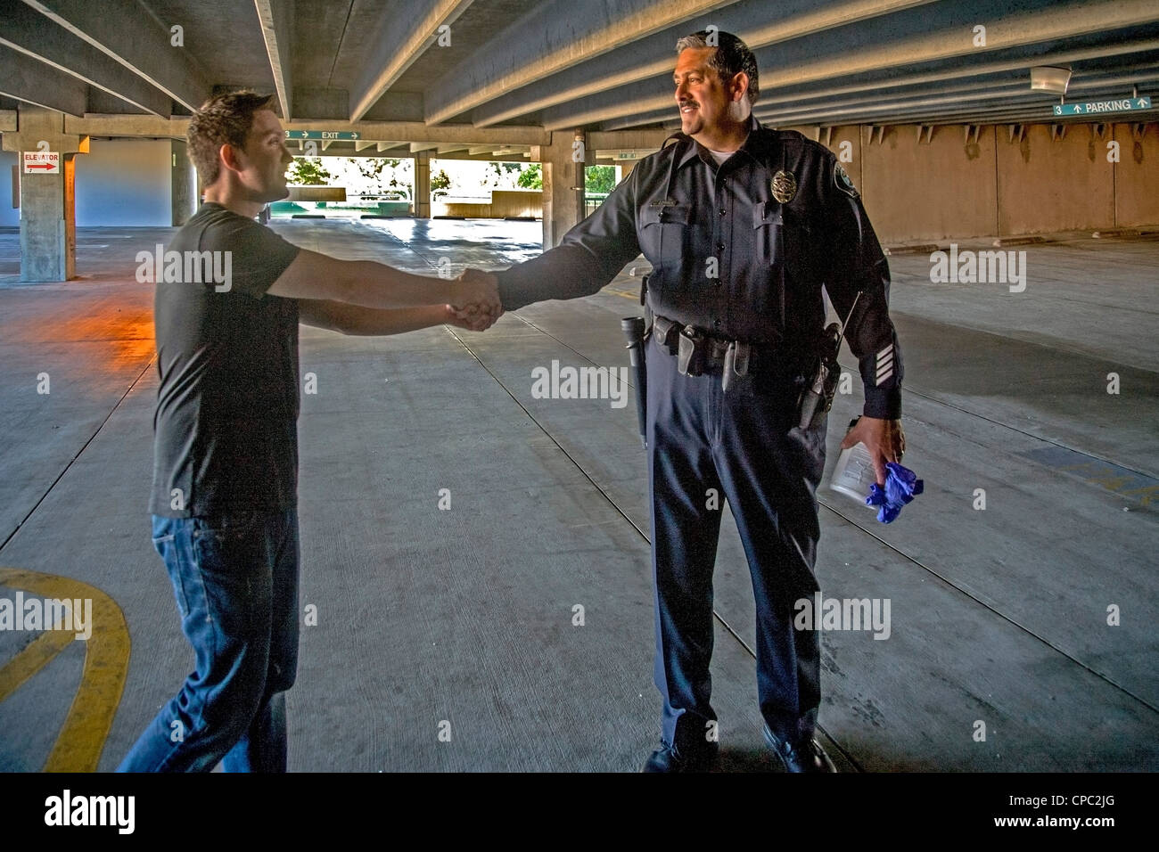 a Hispanic Santa Ana, CA, police officer shakes hands with the appreciative owner of a car that was broken into and robbed. Stock Photo
