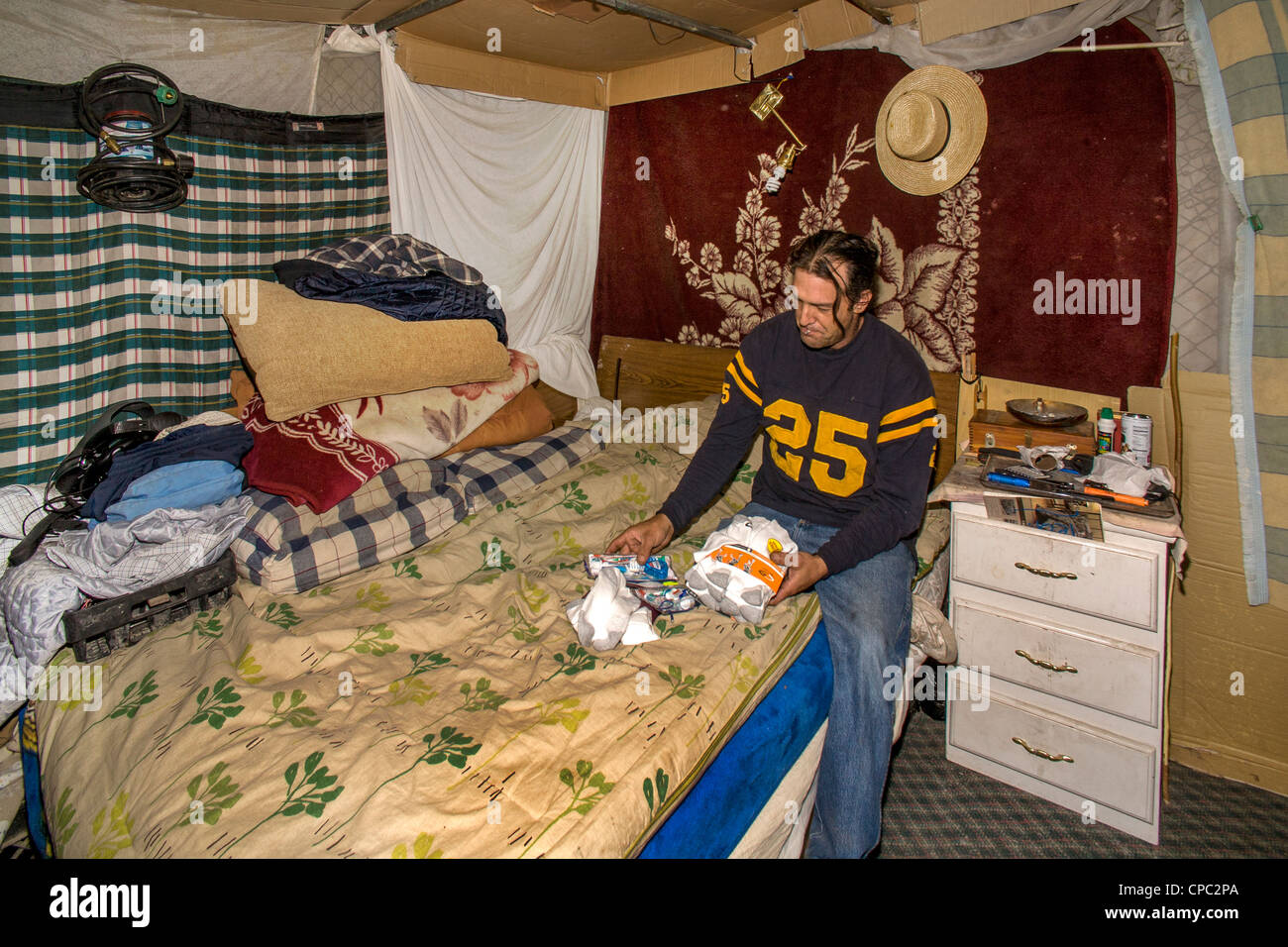 Veteran sits in makeshift shelter in a primitive outdoor encampment in a desert town in California. Stock Photo