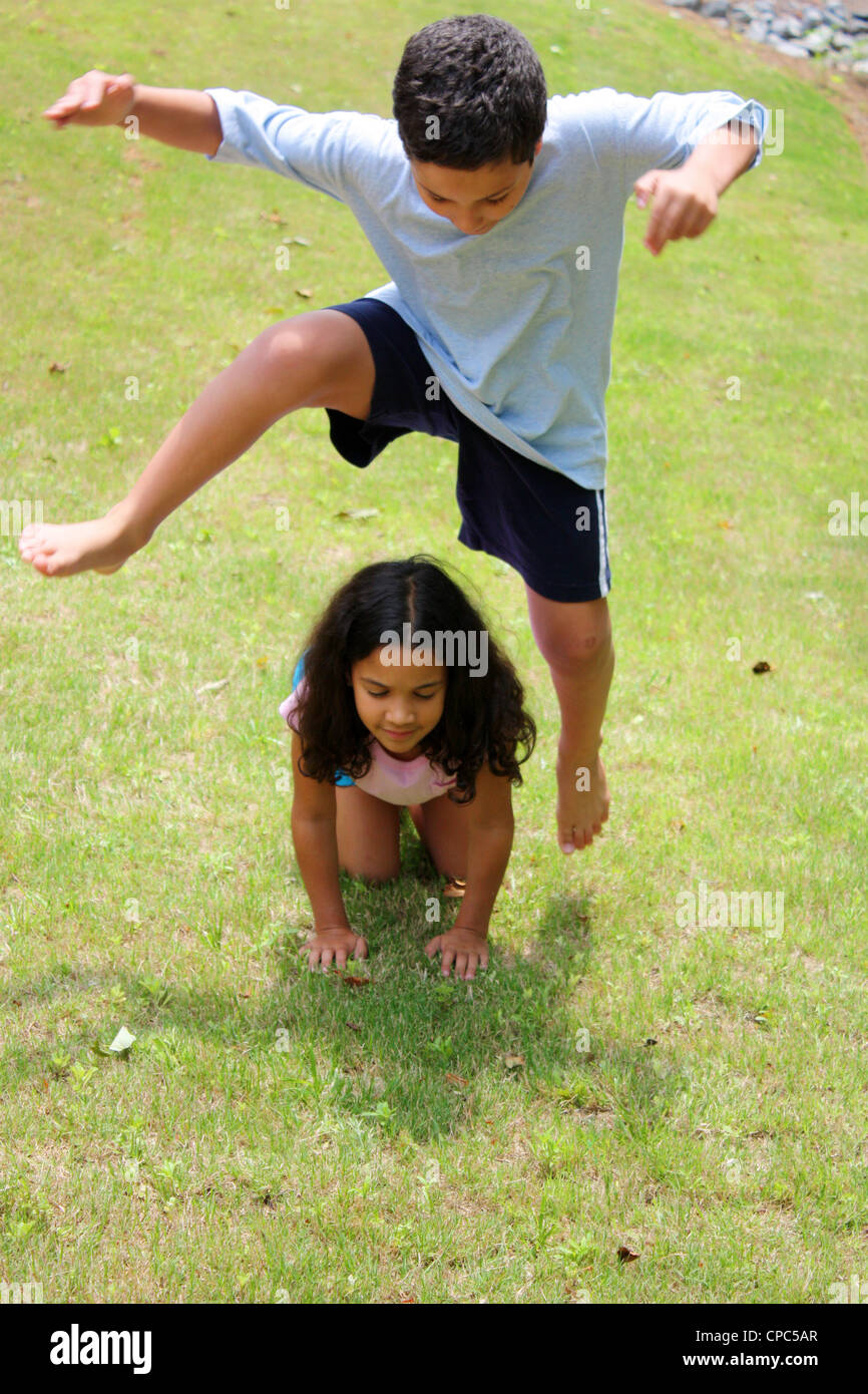 Girl and Boy playing leapfrog outside in the grass Stock Photo