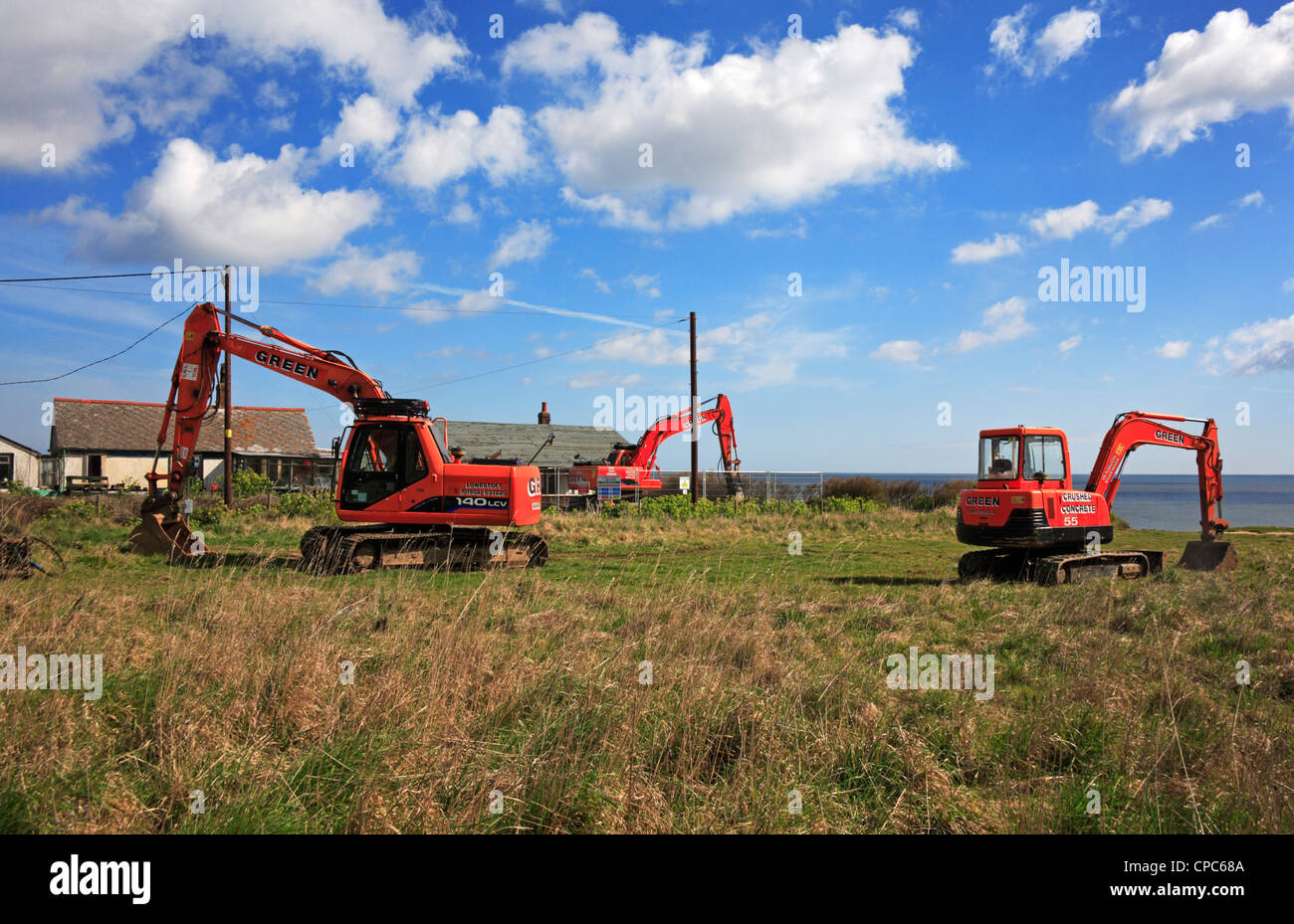 Three diggers on standby at Happisburgh, Norfolk, England, United Kingdom, waiting to demolish cliff edge properties. Stock Photo