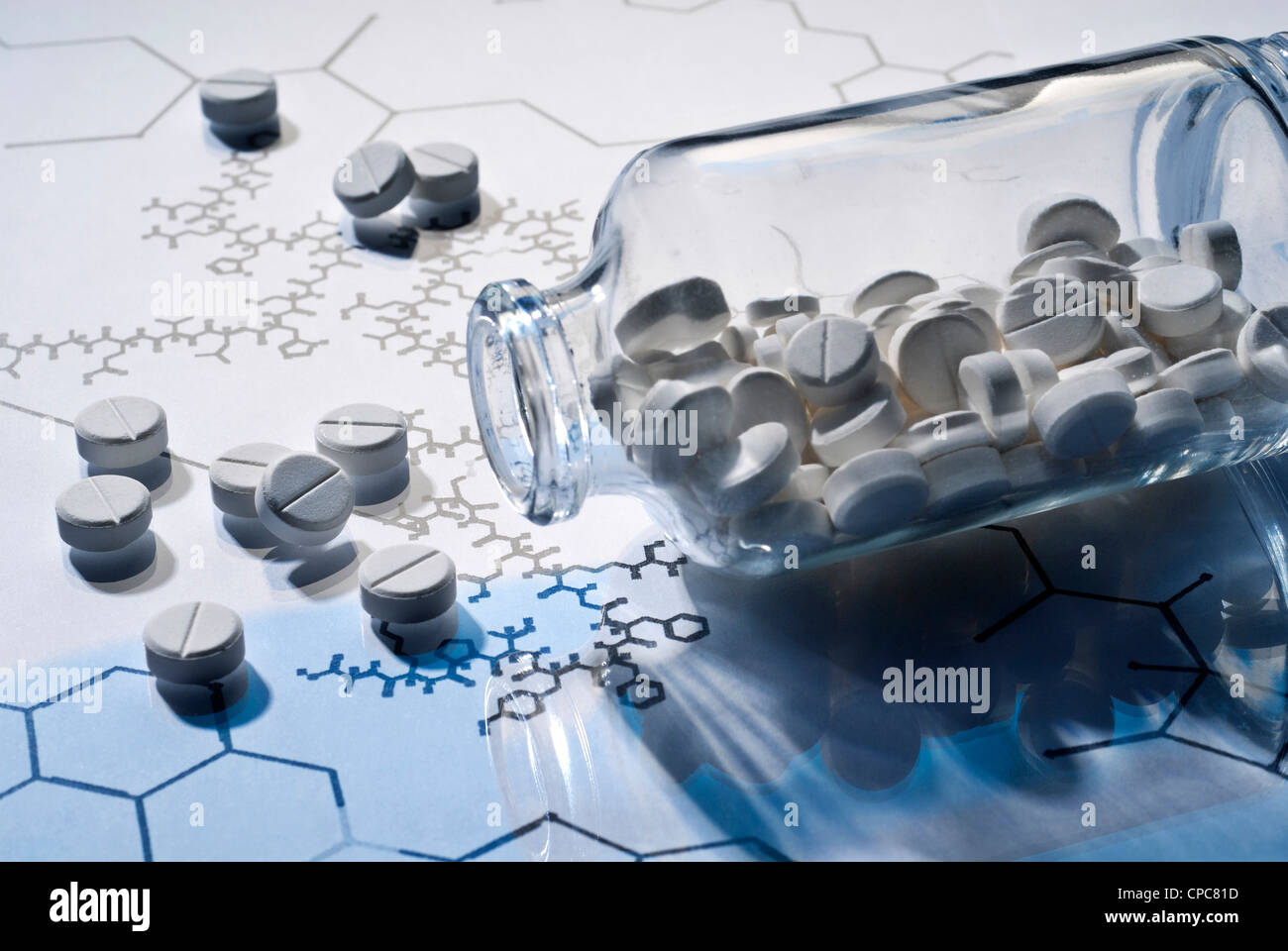 Glass container and tablets on a reflective surface with structural formulas. Stock Photo