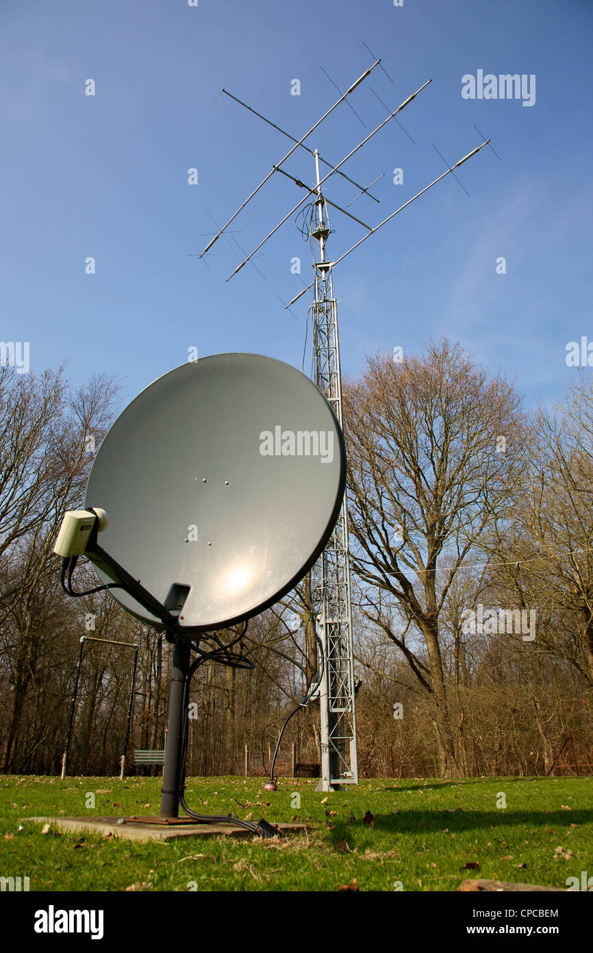 Satellite dish and three element HF radio transmitting mast with Yagi and HF beam Antenna set against a blue sky Stock Photo