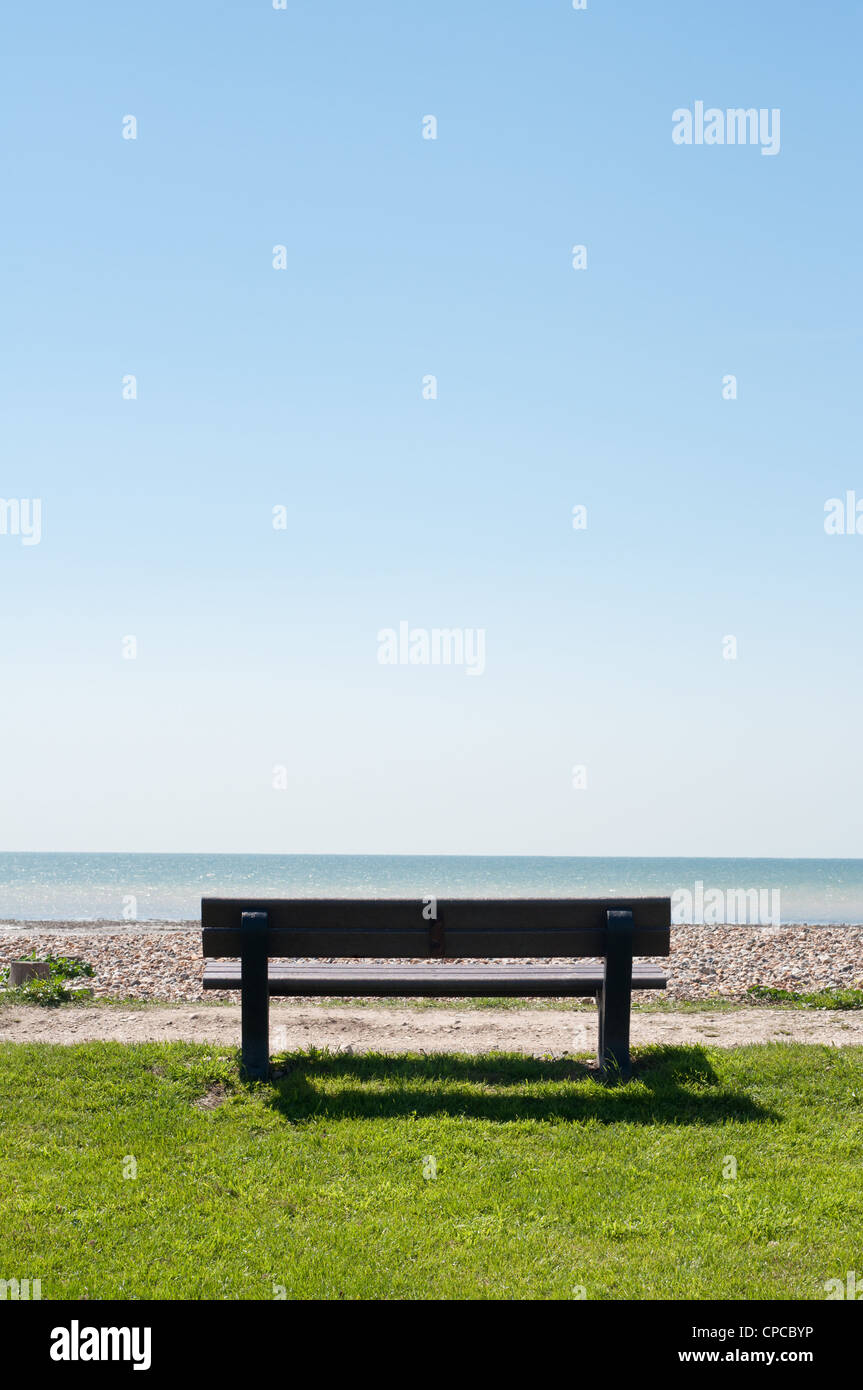 An empty bench viewed from behind, facing the sea with blue sky providing copy space. Stock Photo