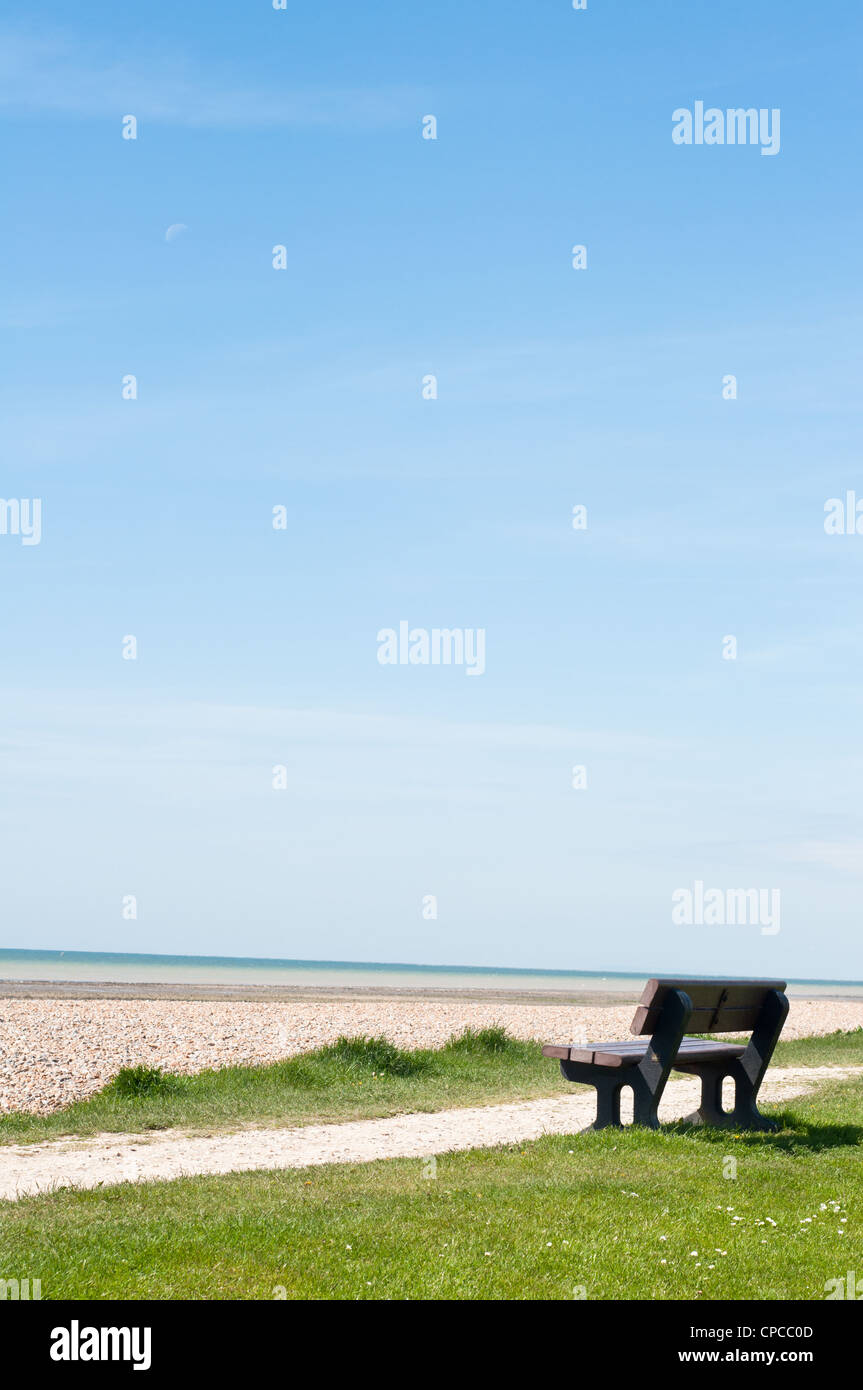 An empty wooden bench on a coastal path, facing the sea with blue sky providing copy space. Stock Photo