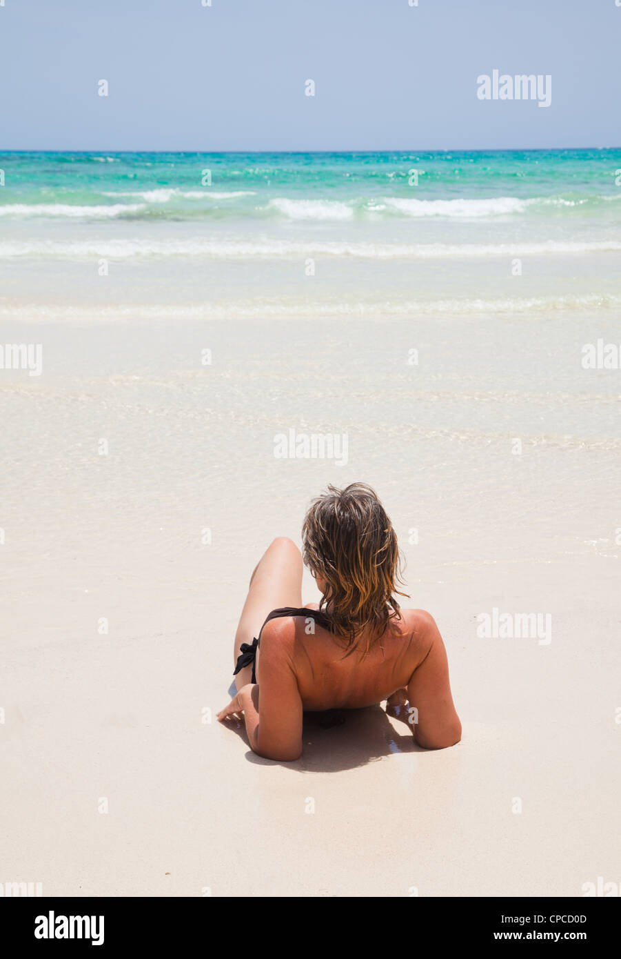 tanned fit middle-age woman is resting after a swim by the edge of the water Stock Photo