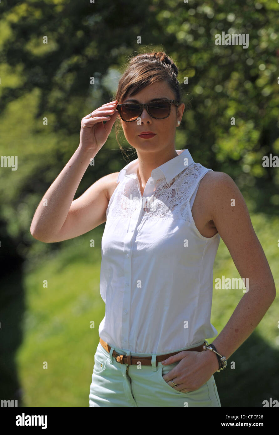 Young woman in spring sunshine wearing pastel colours pale green jeans  white sleeveless top and dark sunglasses UK Stock Photo - Alamy
