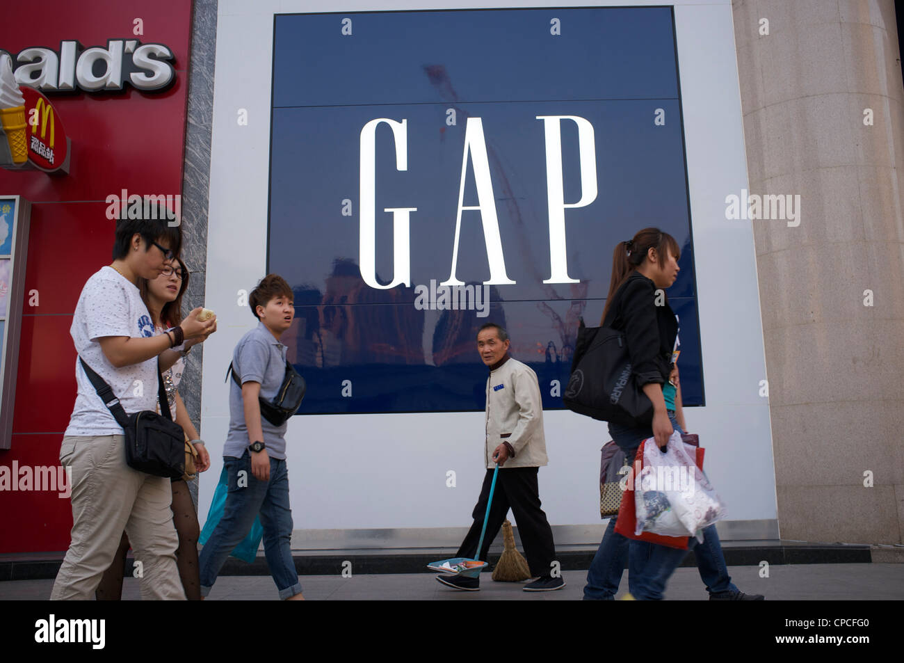 A Chinese elder cleaner and young people walk past clothing retailer GAP logo in Tianjin, China. 14-May-2012 Stock Photo