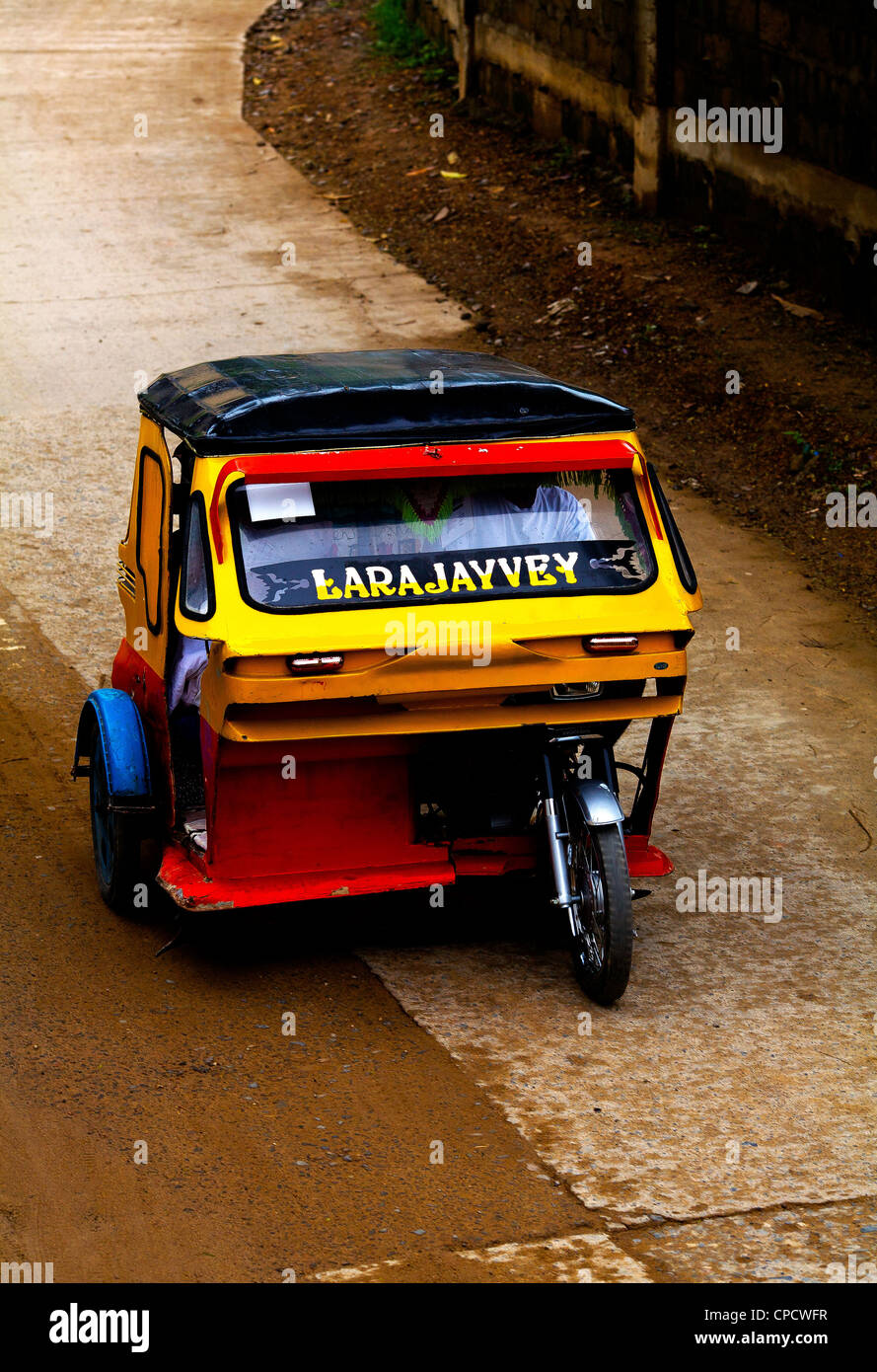 A yellow and red tricycle taxi speeds down the main street of the town of El Nido on the island of Palawan in the Philippines. Stock Photo