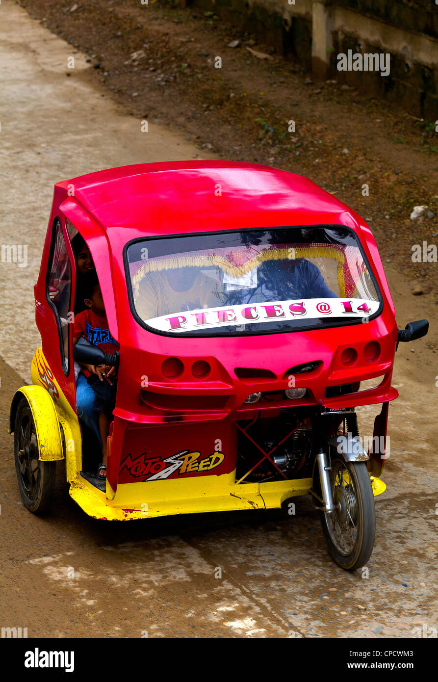 A red and yellow tricycle taxi speeds down the main street of the town of El Nido on the island of Palawan in the Philippines. Stock Photo