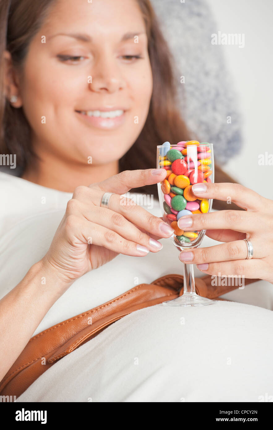 Pregnant woman holding a glass filled with colorful candy on her
