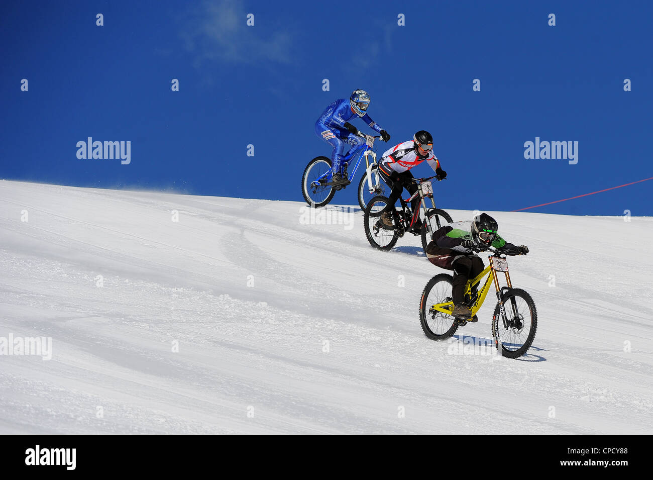 Downhill mountain bikers race at speed on snow during the Saas Fee Glacier Bike race in Switzerland. Stock Photo