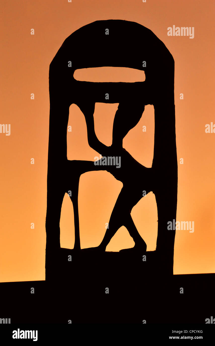 Wooden sculpture of African woman silhouetted against orange sky at sunset Stock Photo