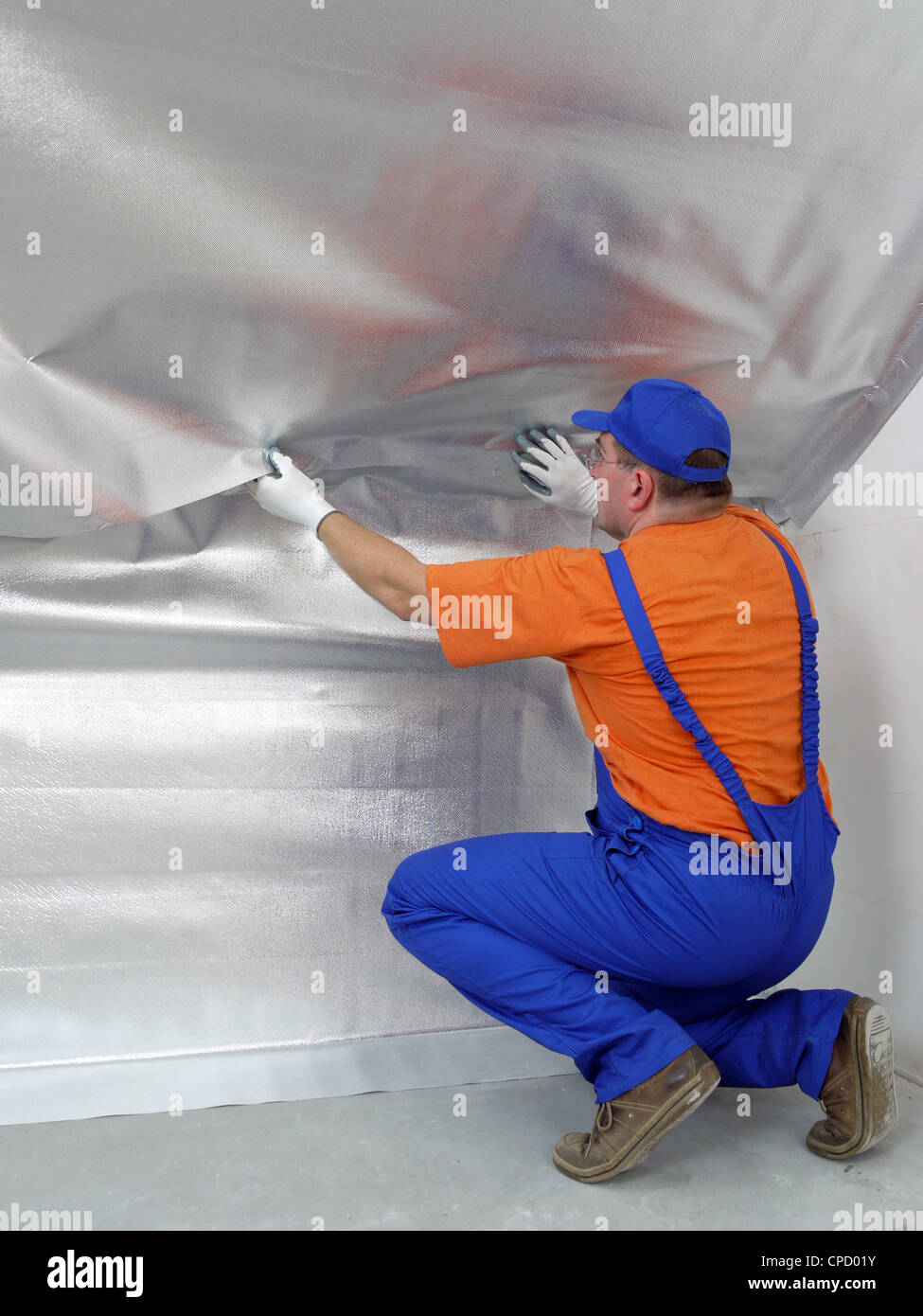 Construction worker affixing vapor insulation foil under thermally insulated attic surface Stock Photo